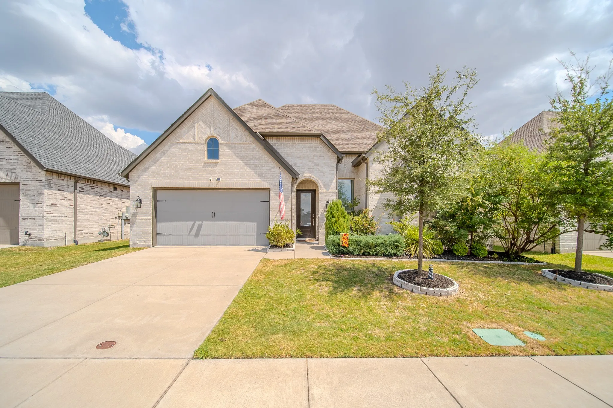 Stone façade with a gabled roofline, concrete driveway, attached garage, and mature landscaping