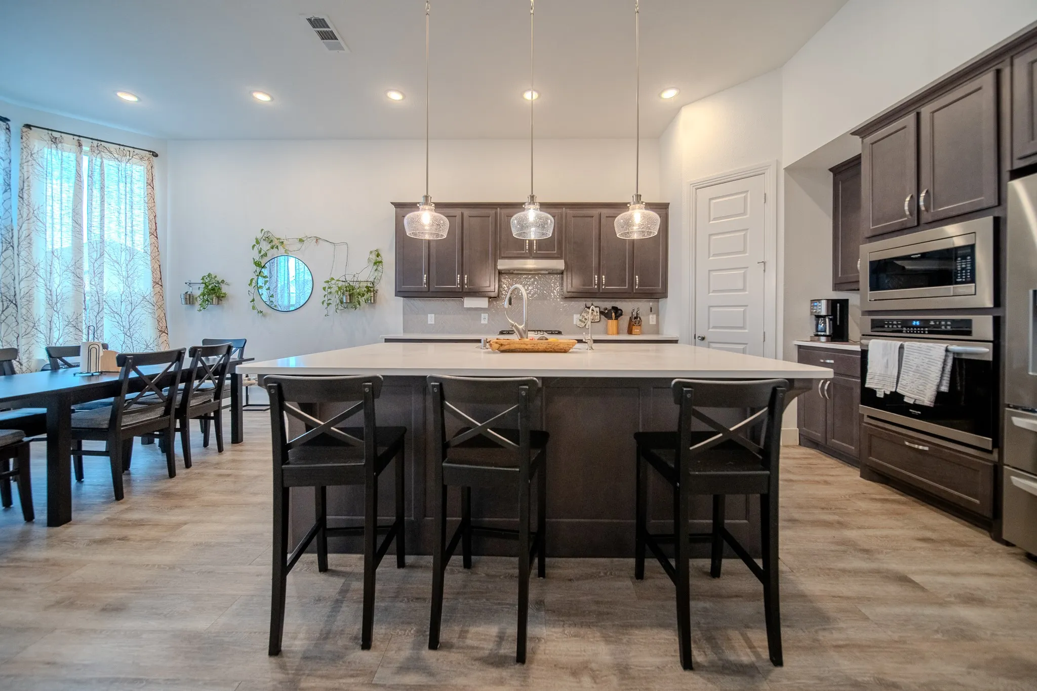 Spacious kitchen featuring an expansive island with seating, stainless steel appliances, dark wood-finish cabinetry, and wood-finish flooring