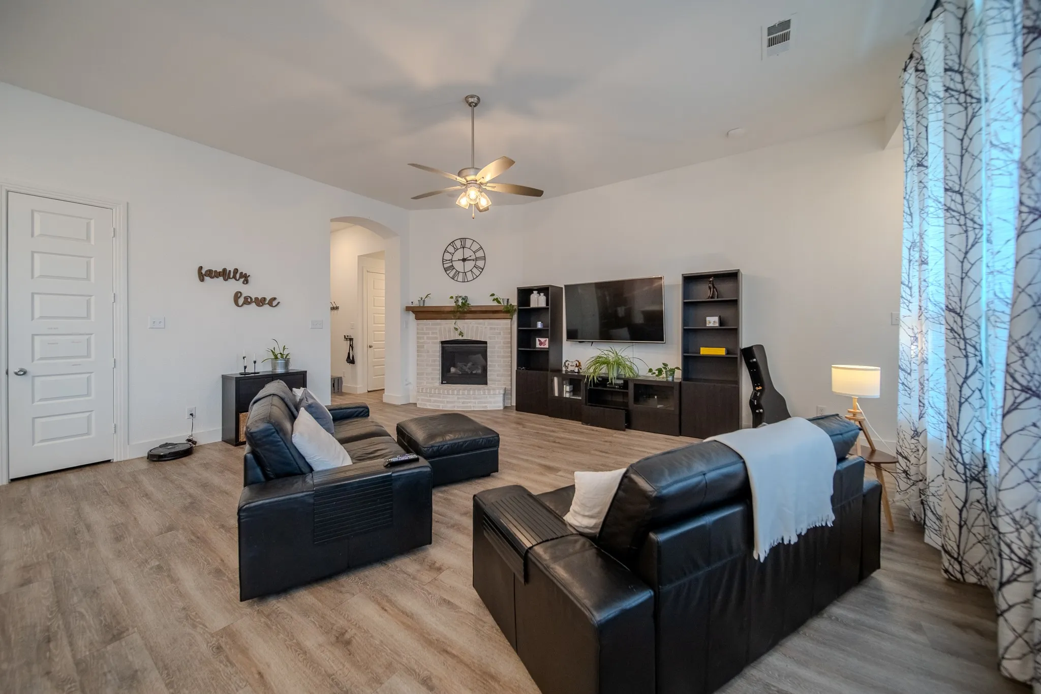 Wood-finish flooring, white brick fireplace with wood mantel, ceiling fan, arched doorway, and five-panel interior door