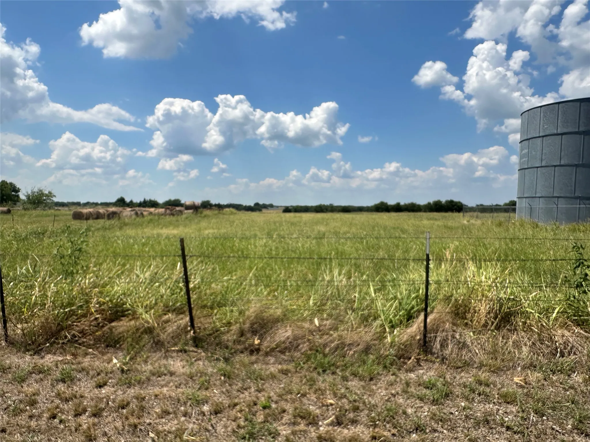 Expansive open field with natural grasses, featuring a partial view of a metal grain silo