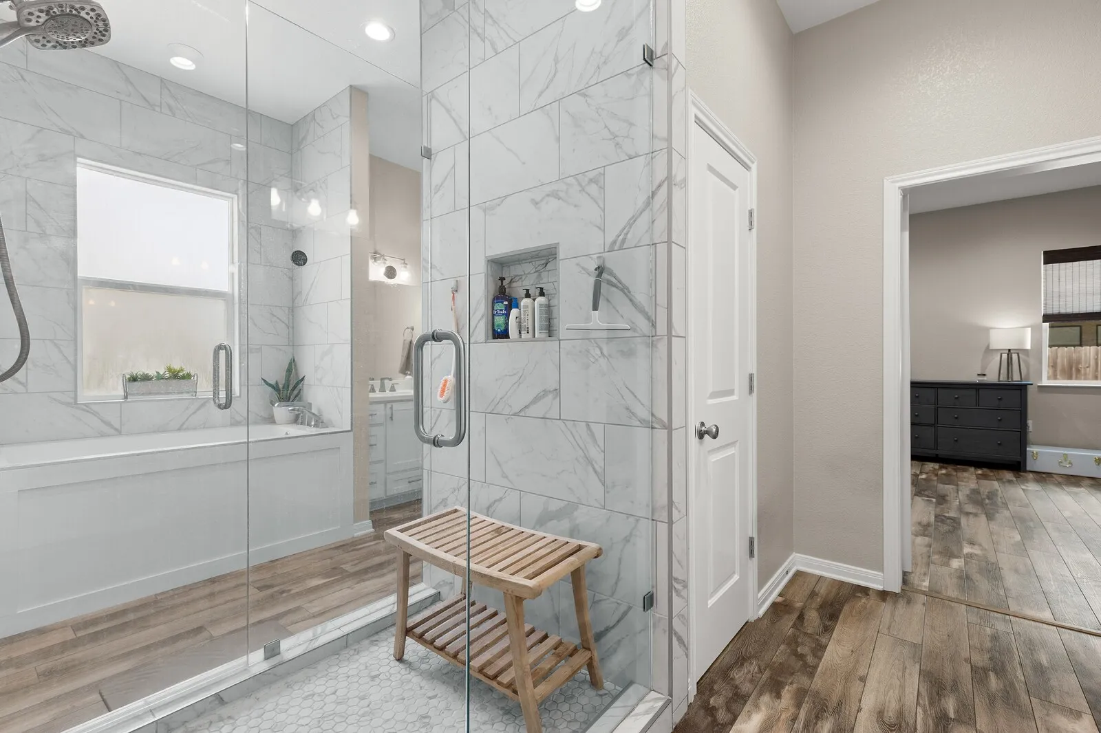 Glass-enclosed shower with white tiled walls, hexagonal shower floor, and built-in niche