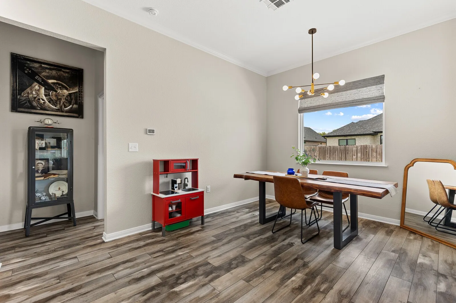Wood-finish flooring throughout, crown molding, modern chandelier, and a window with blinds