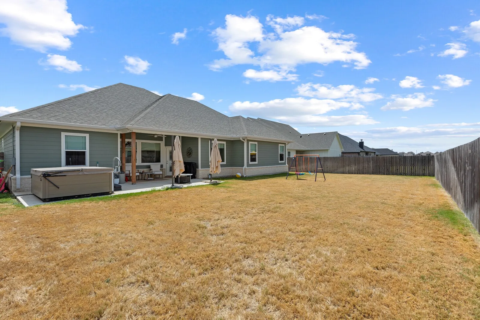 Expansive backyard with a full privacy fence, covered patio, and hot tub