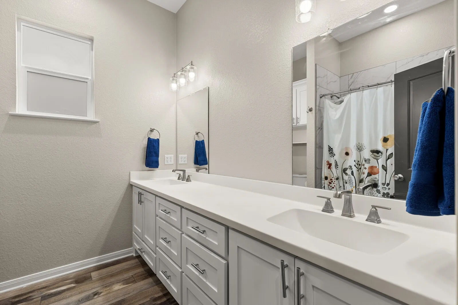 Dual vanity with integrated sinks, brushed nickel fixtures, light-toned cabinetry, and wood-finish flooring
