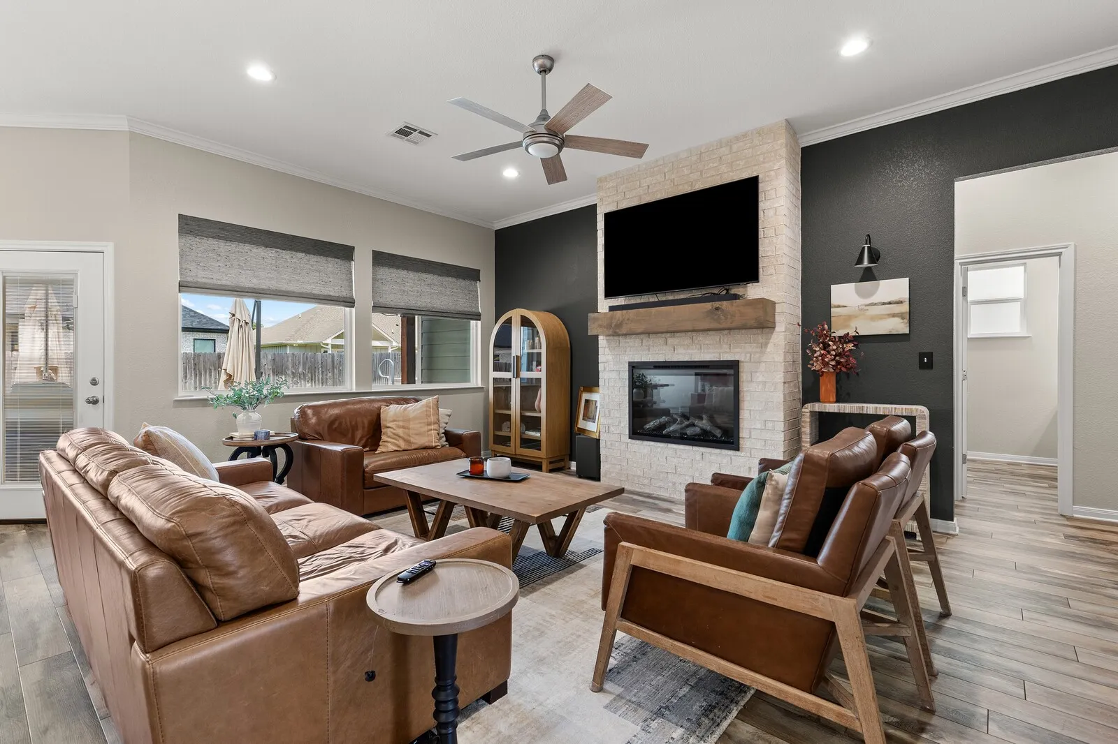 Living area featuring wood-finish flooring, a white brick-finish fireplace with a wood-beam mantel, recessed lighting, and a ceiling fan