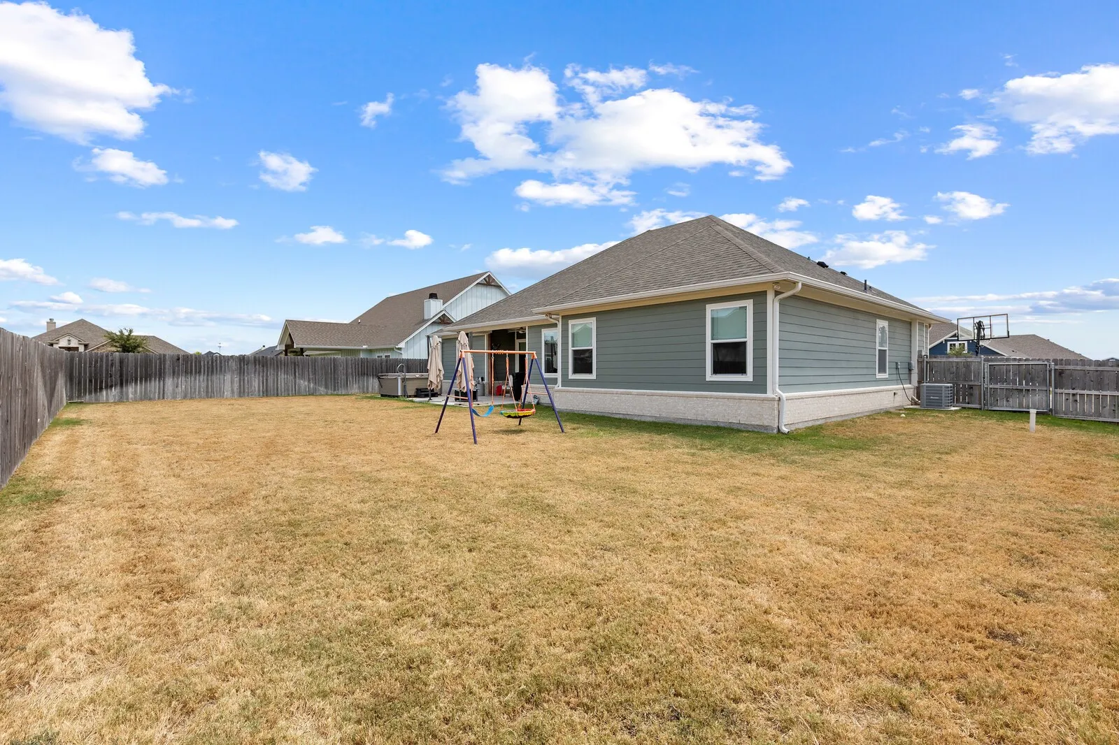 Expansive fenced backyard featuring a single-story residence with a gabled roof, horizontal siding, and white trim windows