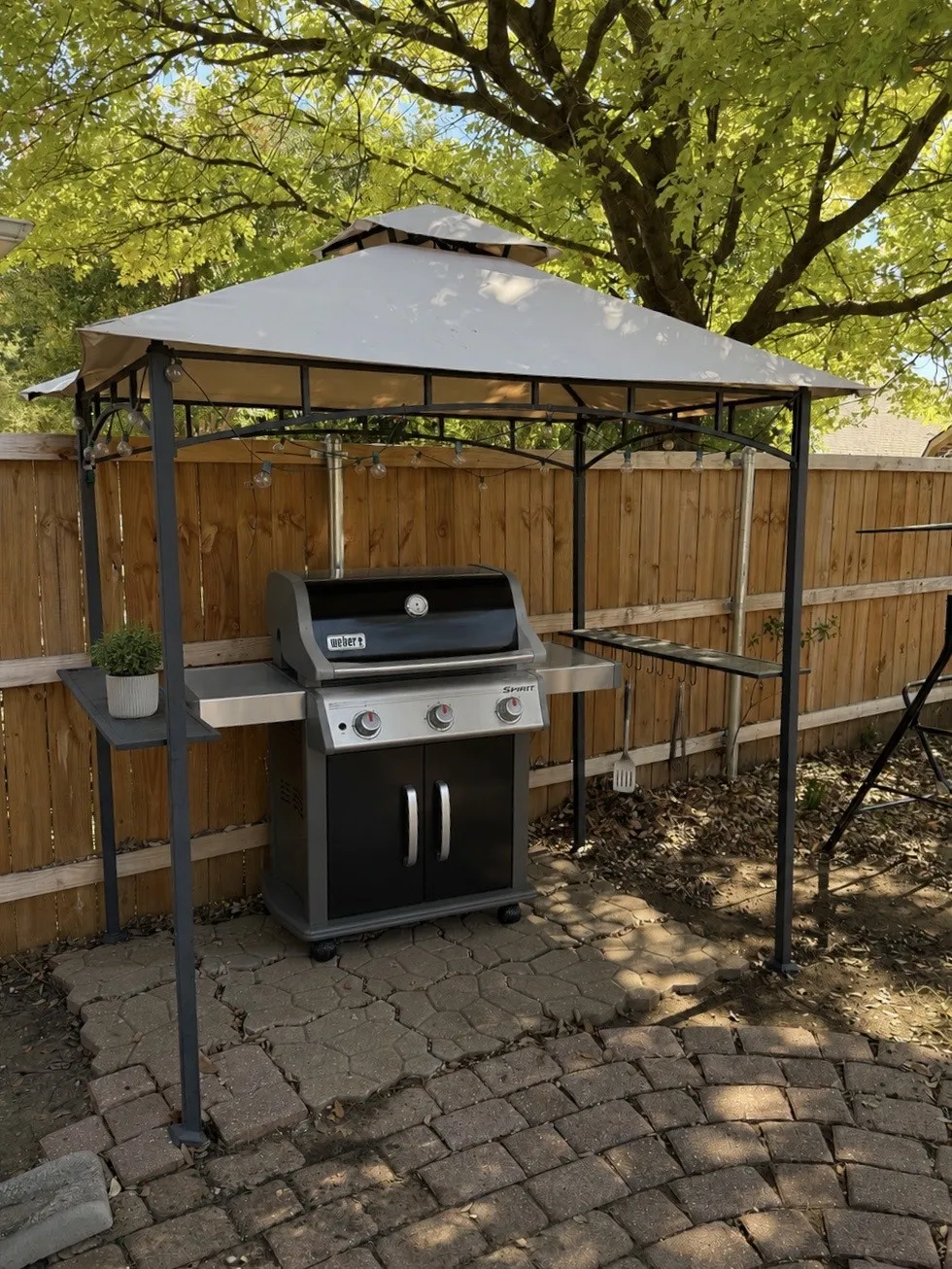 Patio area featuring a fabric-covered pergola with metal framing, wood privacy fencing, and paver stone flooring