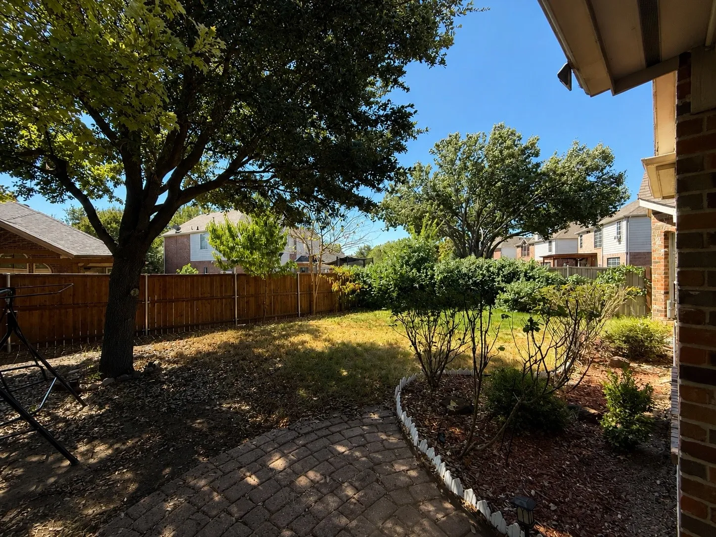 Expansive backyard featuring a brick paver patio, a full-grown tree, manicured landscaping, and a privacy fence