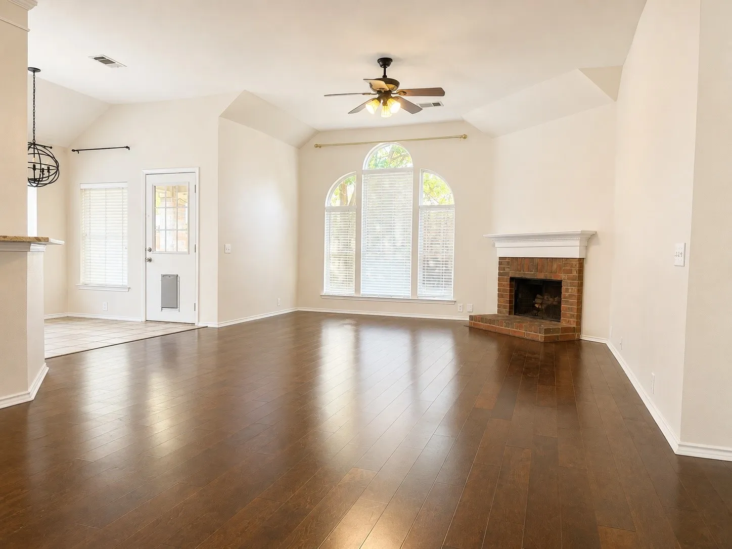 Vaulted ceilings with a ceiling fan, wood-finish flooring, brick fireplace with a mantel, arched window, and tiled flooring