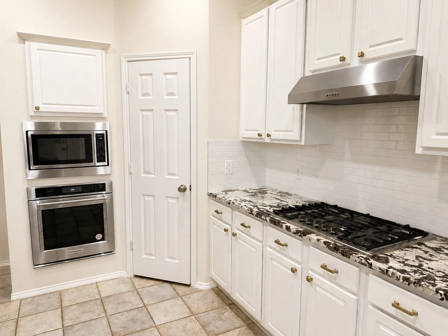 White cabinetry, granite countertops, subway tile backsplash, stainless steel gas cooktop, and built-in stainless steel oven and microwave