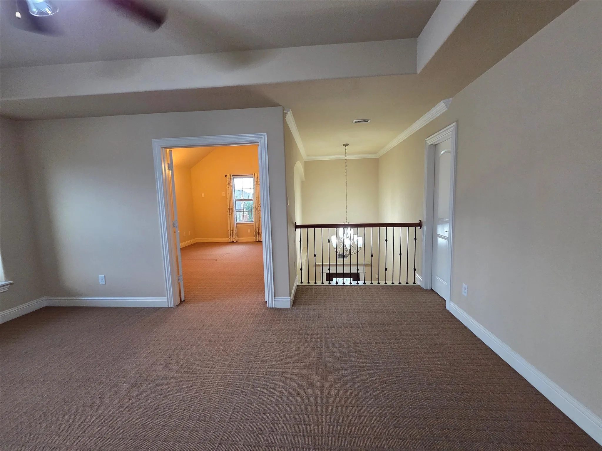 Carpeted loft area with wrought iron baluster railing, white trim, and a ceiling fan