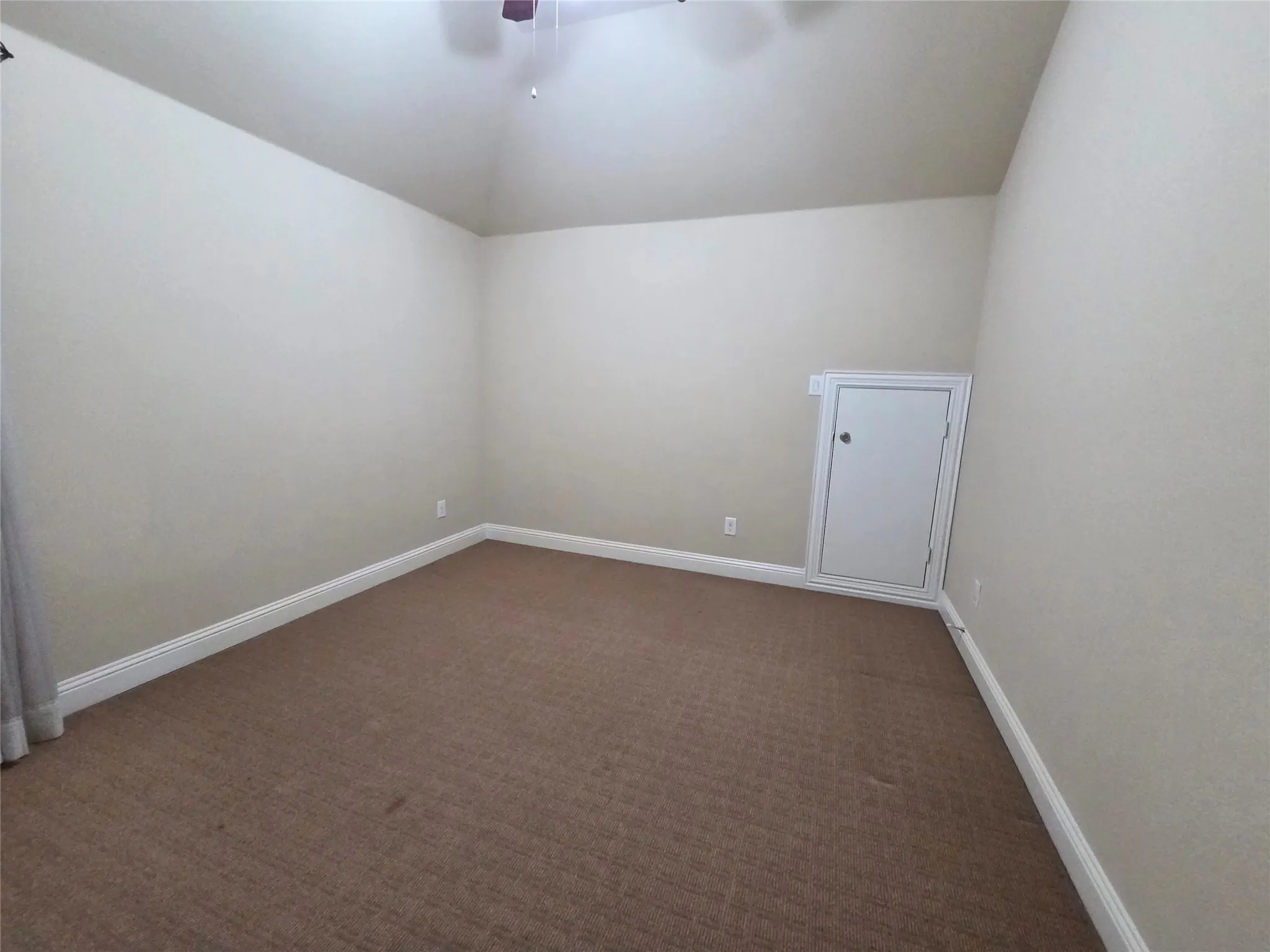 Vaulted ceiling, neutral wall paint, brown carpet flooring, white trim, and a built-in storage access panel