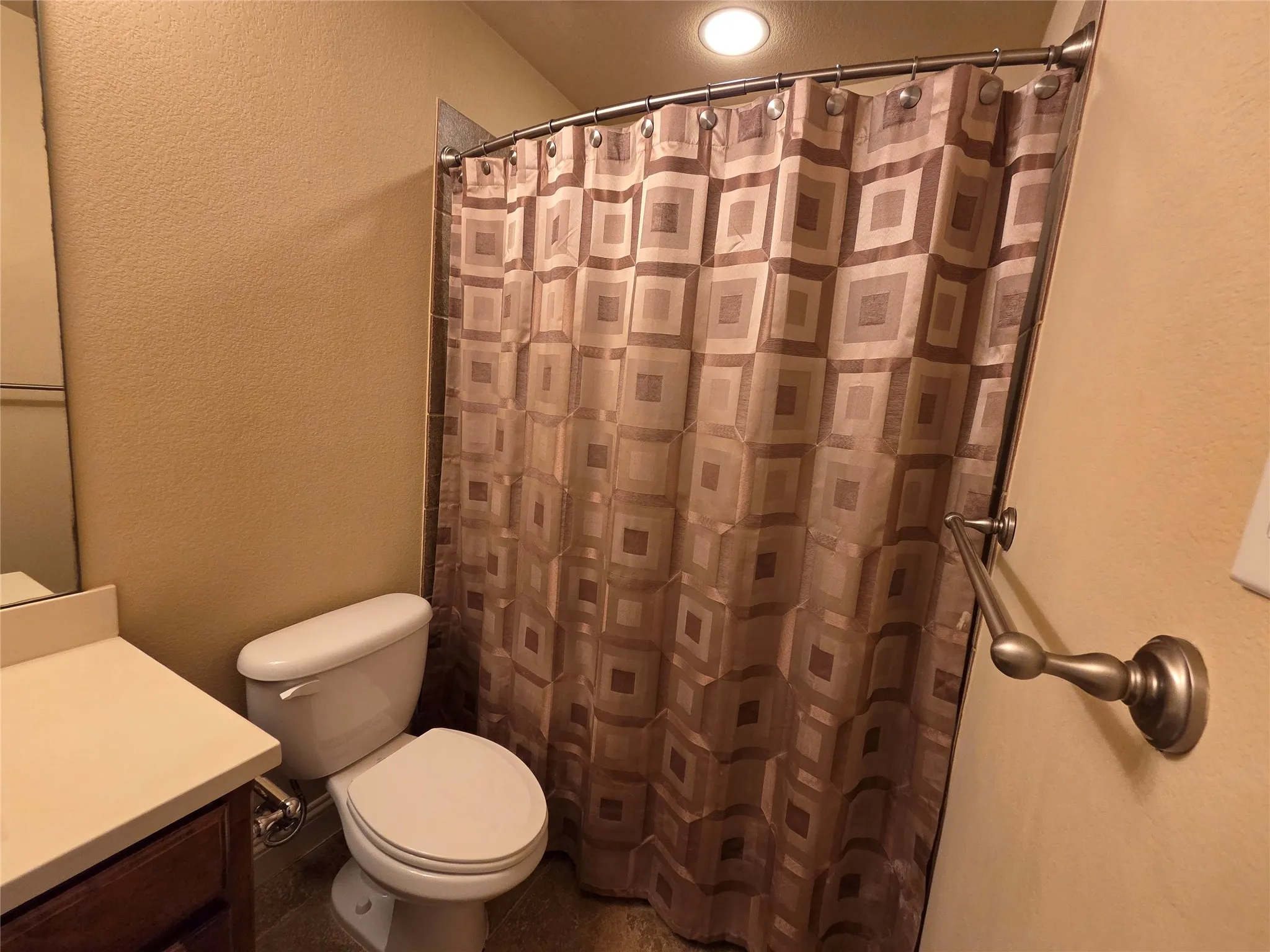 White toilet with a built-in tank, light-colored countertop, and a dark wood-finish vanity