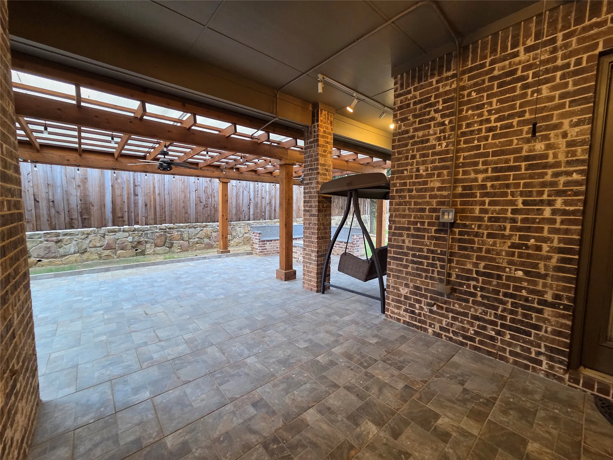 Expansive brick patio featuring paver flooring, a wooden pergola, and a stone retaining wall