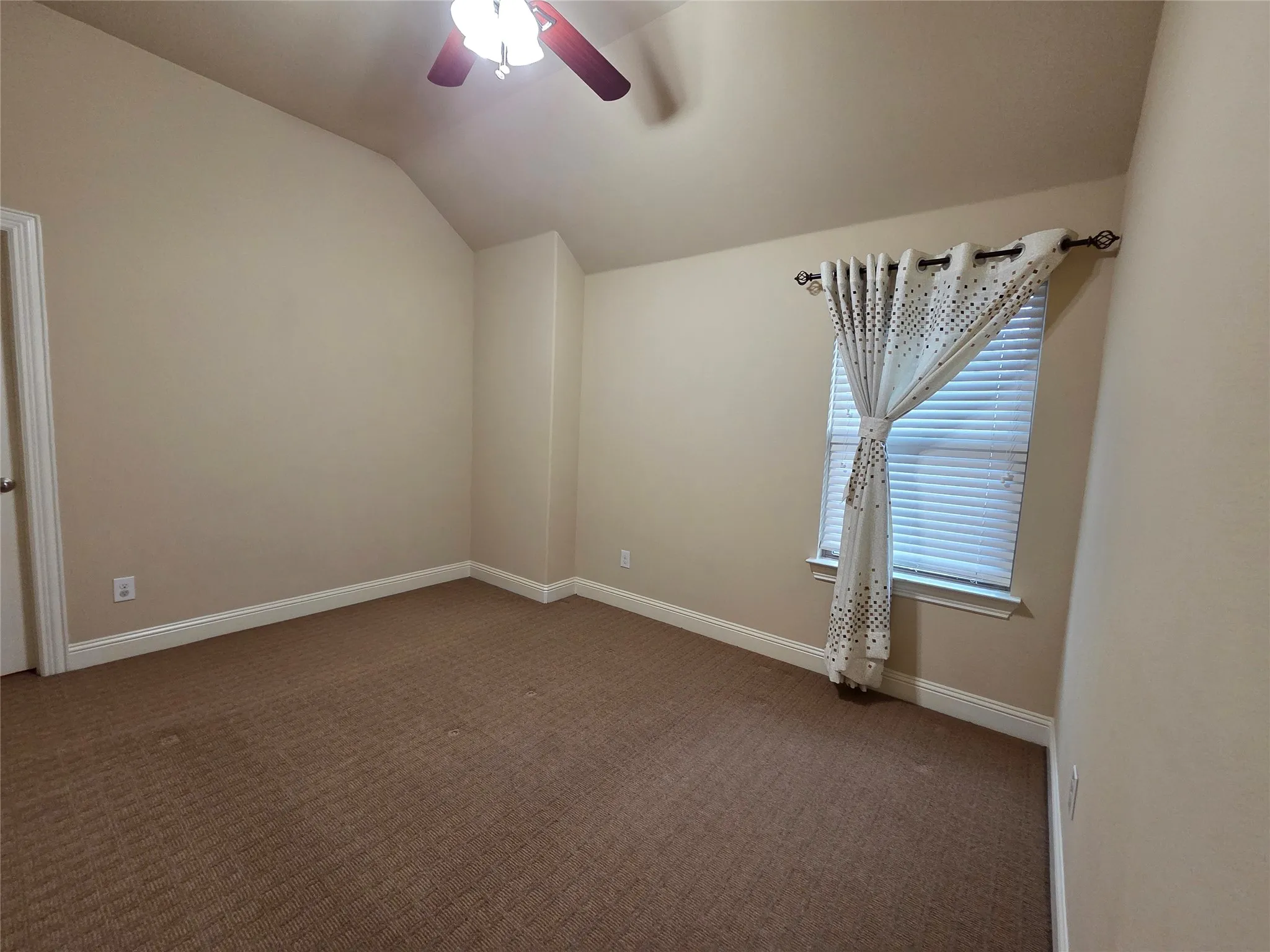 Carpeted room featuring a ceiling fan, vaulted ceiling, and a window with blinds
