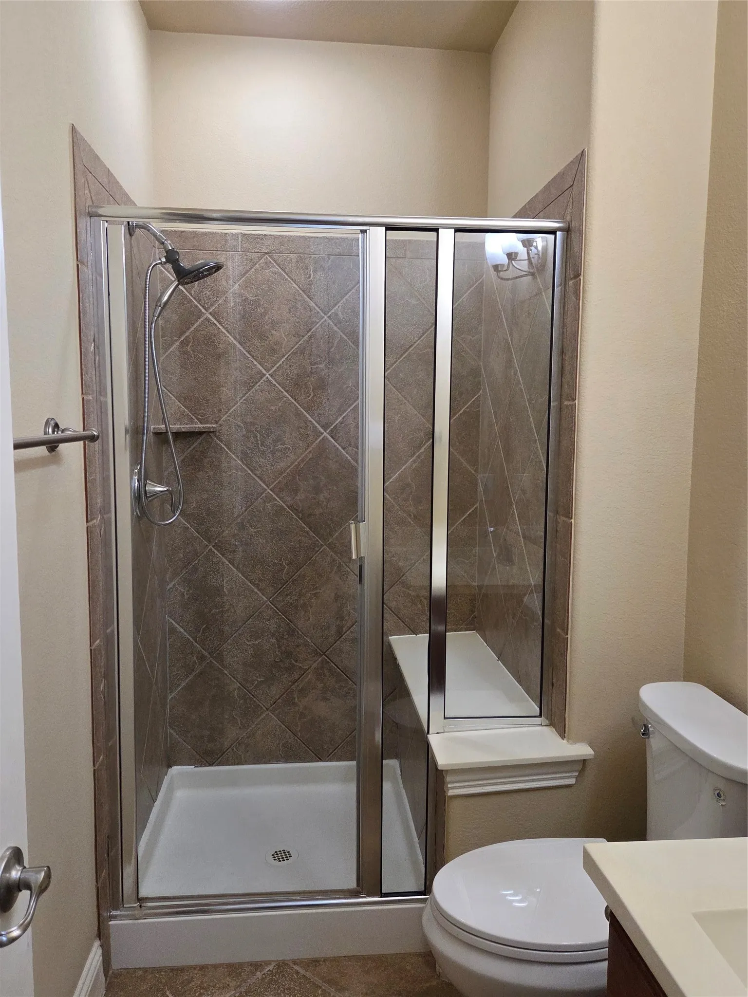 Modern bathroom featuring a frameless glass-enclosed shower with diagonal tile surround, white ceramic pedestal sink, and white porcelain toilet