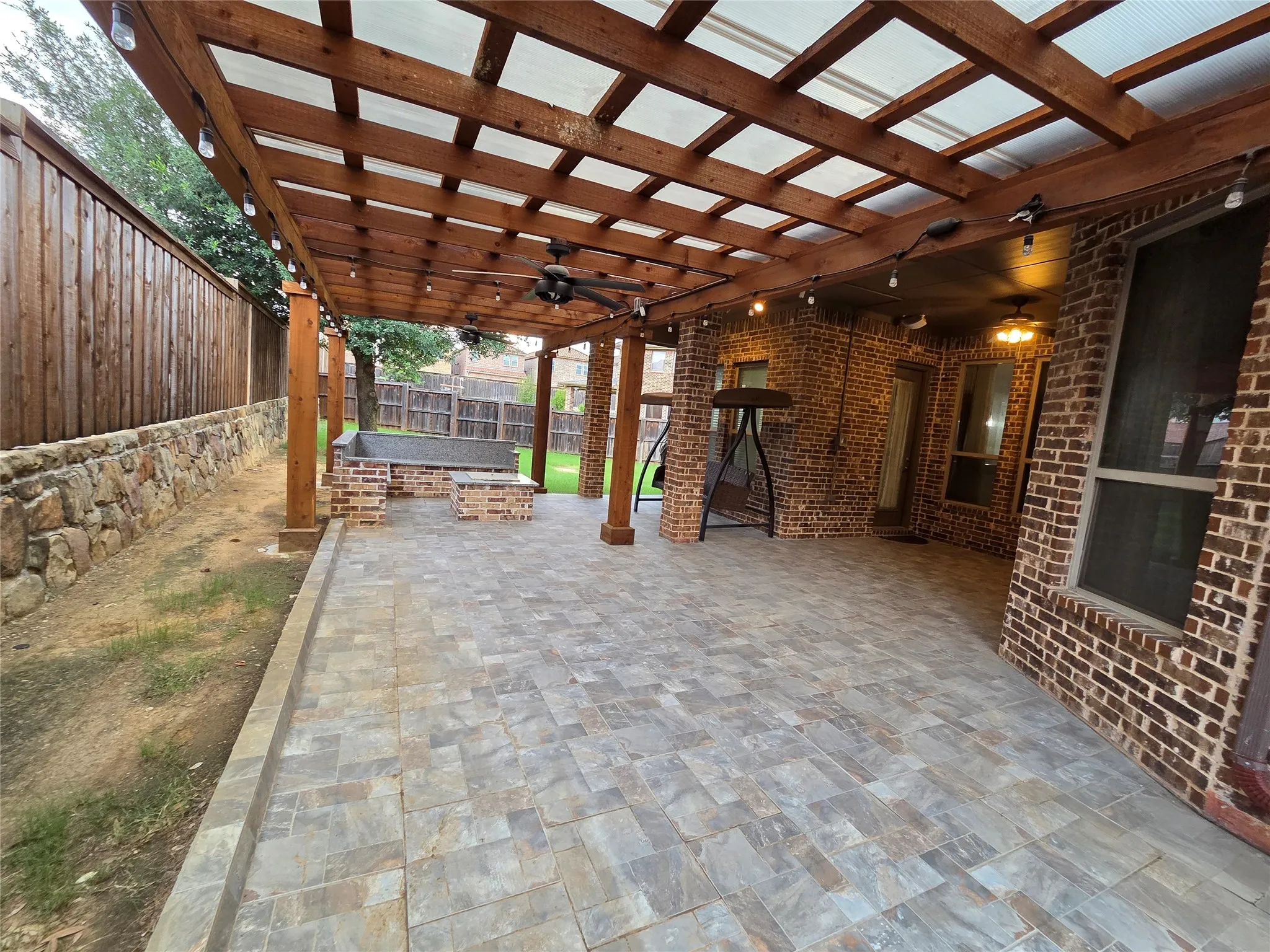 Expansive covered patio featuring a wood pergola with translucent roofing, string lighting, and ceiling fans