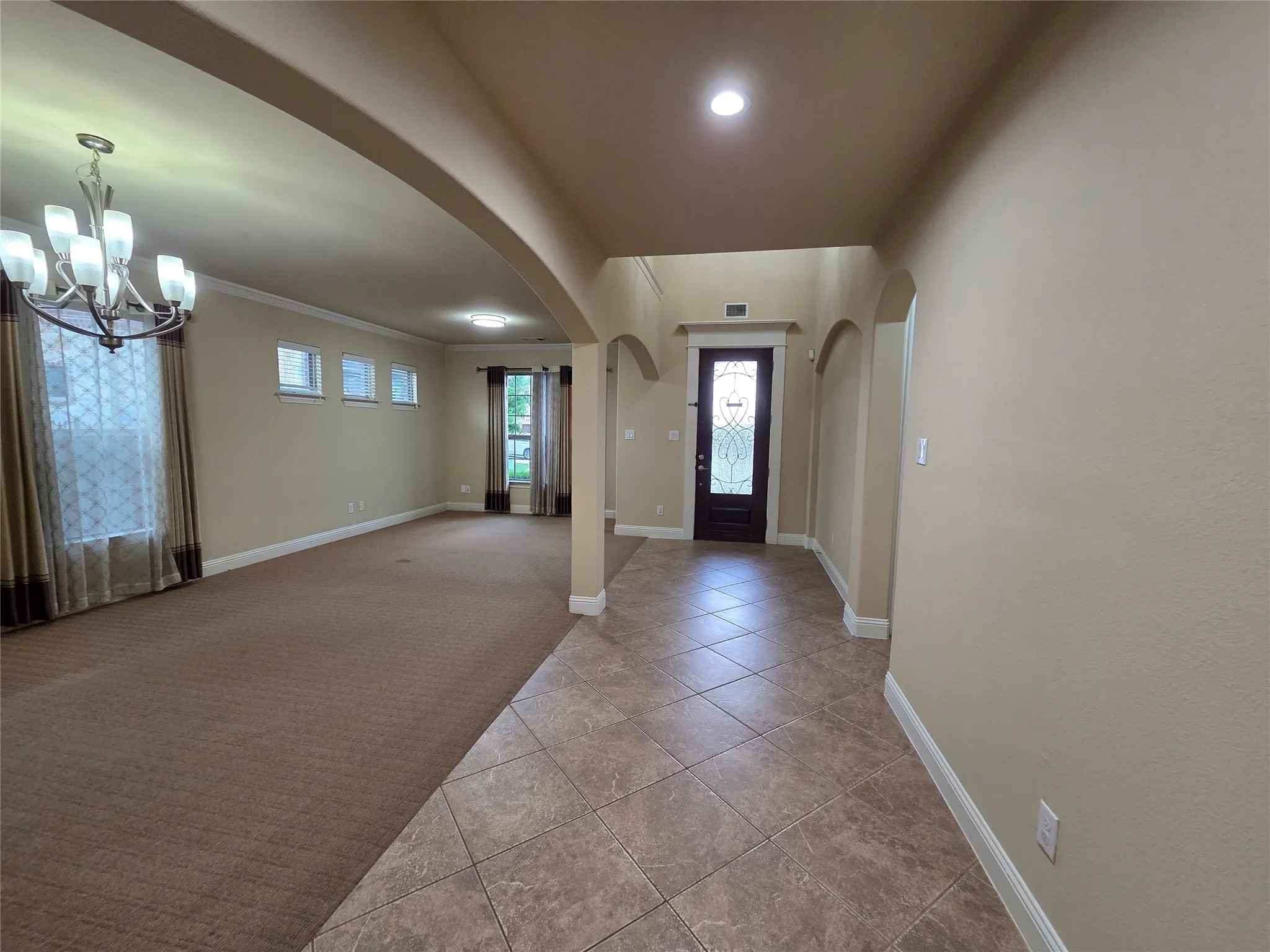 Tiled entryway flooring, arched doorways, an ornate front door, a chandelier, and recessed lighting
