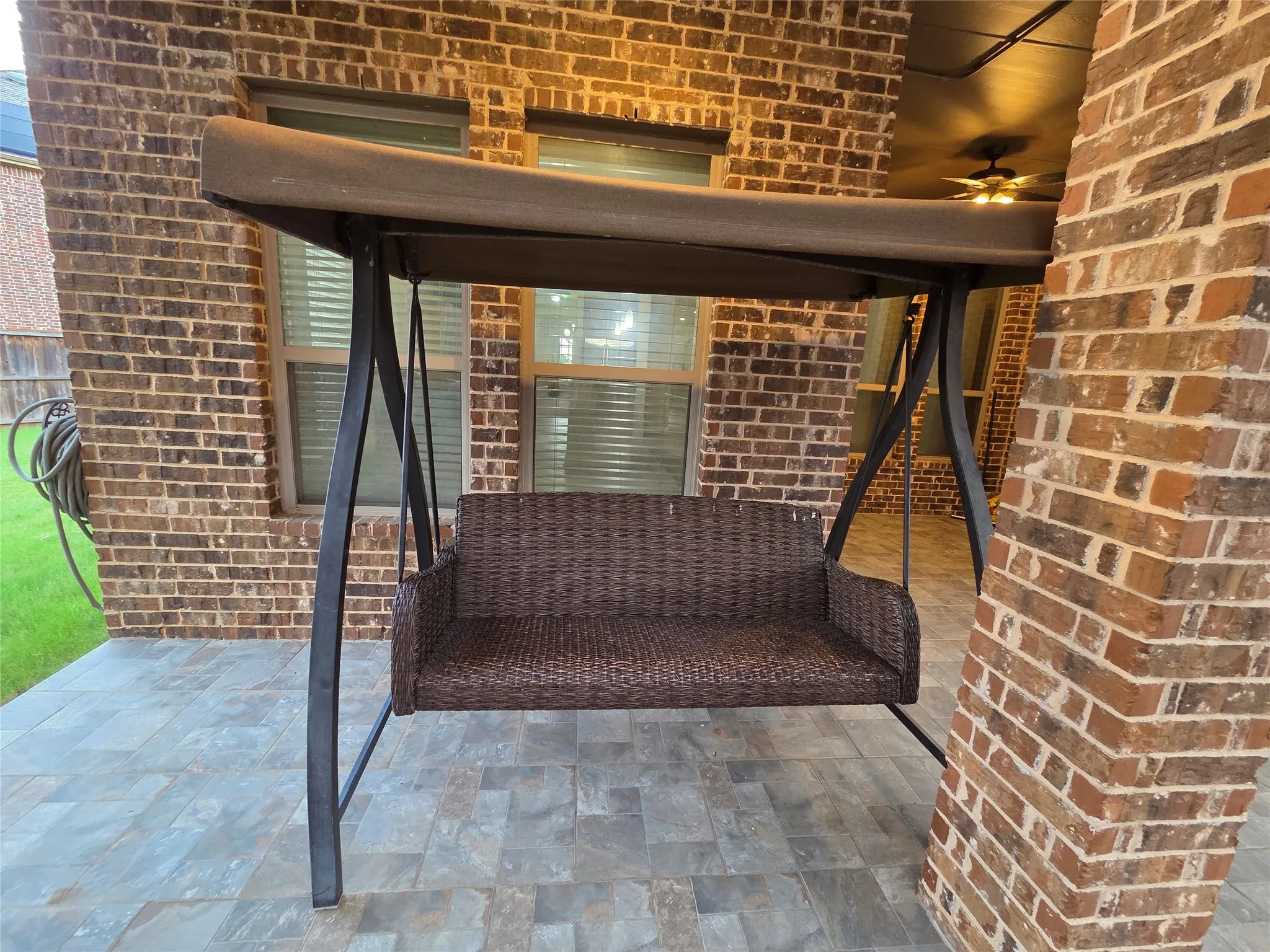 Covered patio featuring a brick exterior, stone tile flooring, and a ceiling fan