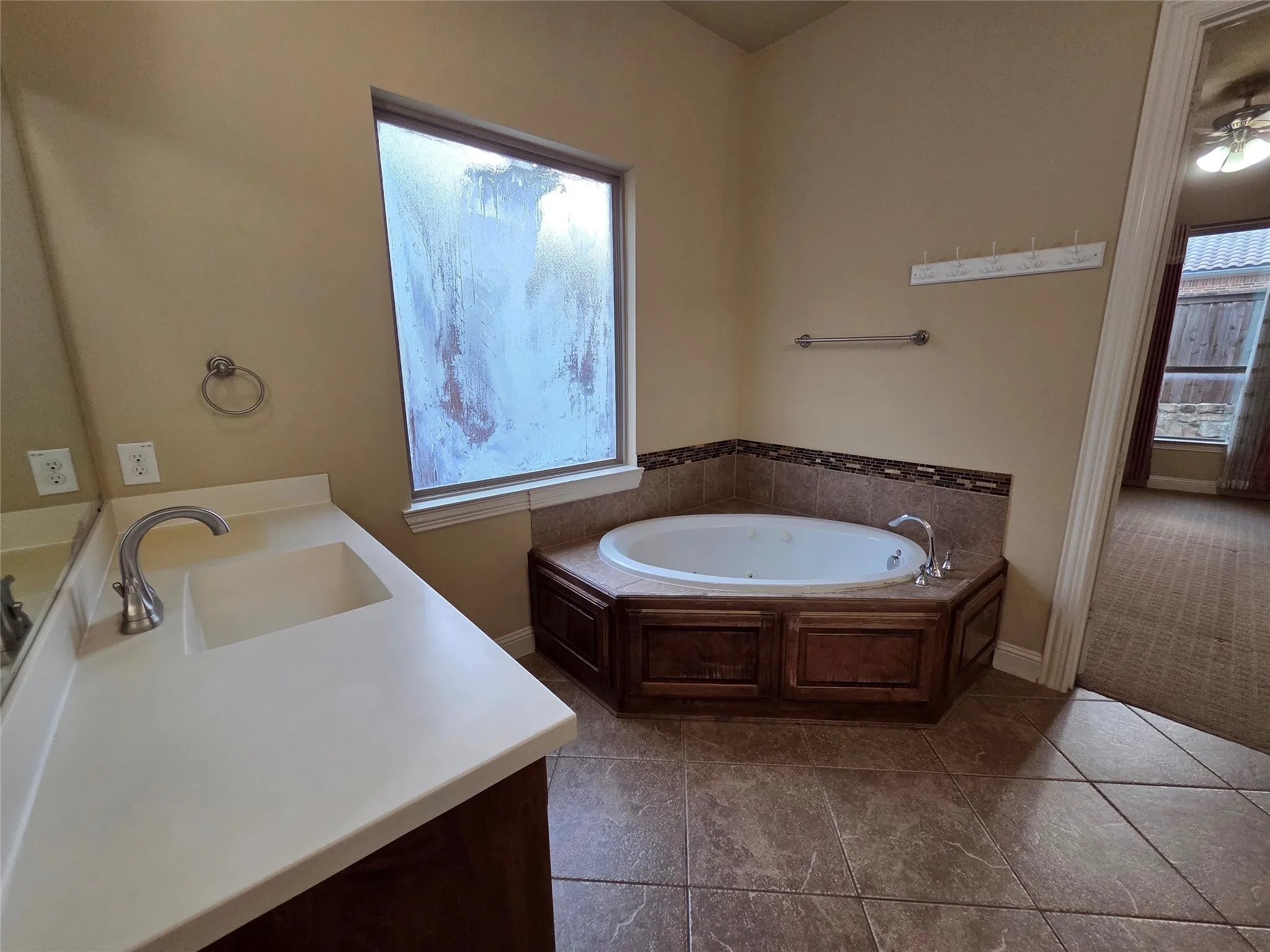 Built-in corner bathtub with tiled surround, wood-finish cabinetry, and a single vanity with an integrated sink and light-toned countertop