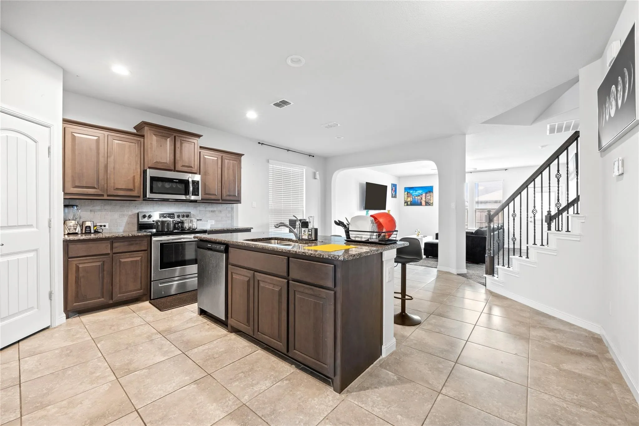 Kitchen featuring recessed lighting, stainless steel appliances, dark wood cabinetry, a center island with a sink, and tile flooring