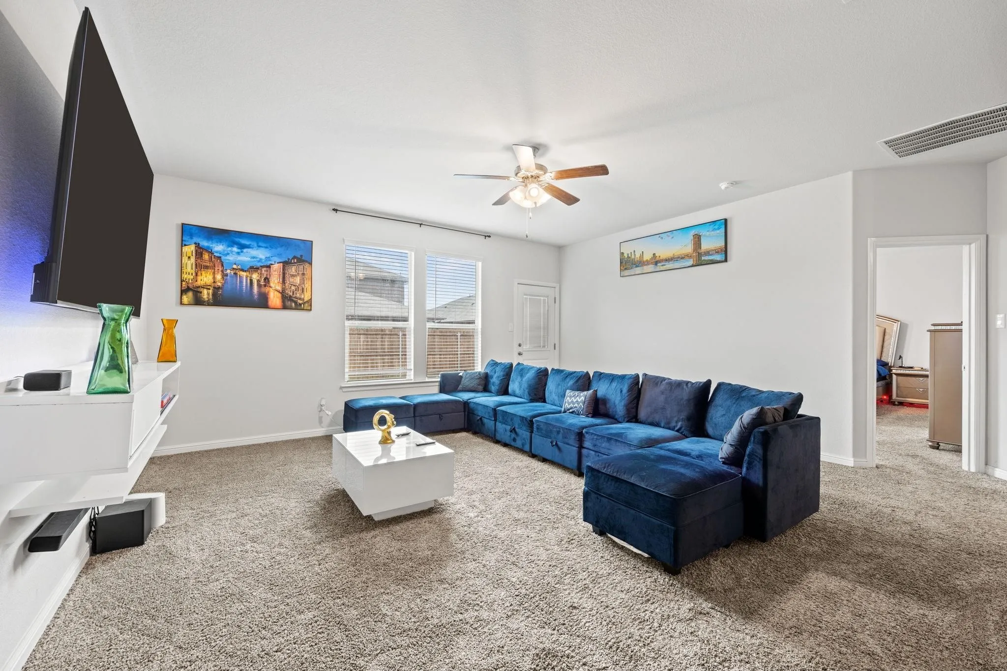 Carpeted living area with a ceiling fan, dual windows, and a built-in floating media console