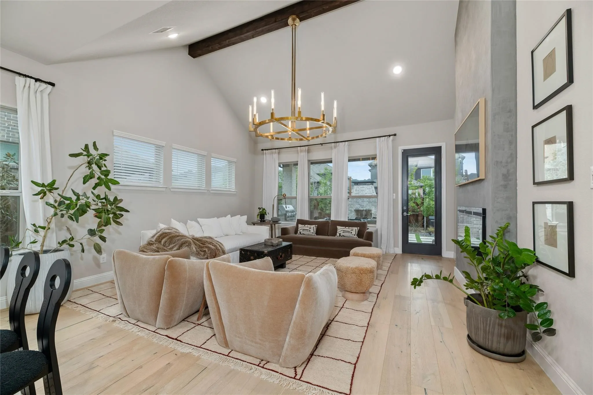 Spacious living area featuring a vaulted ceiling with exposed wood beam, light wood-finish flooring, and a contemporary chandelier