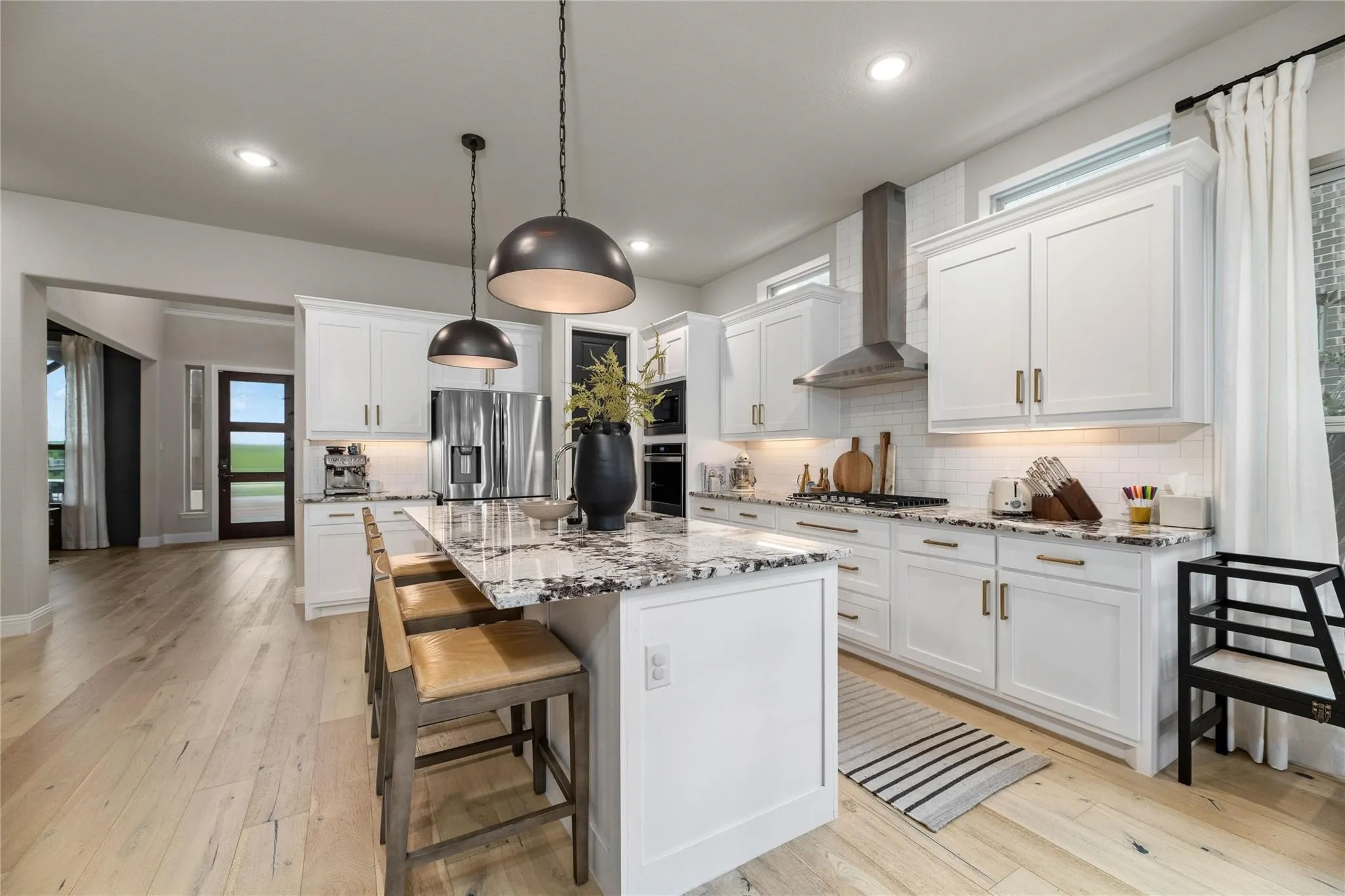 Modern kitchen featuring a large center island with seating, white shaker cabinetry, stainless steel appliances, and wood-finish flooring