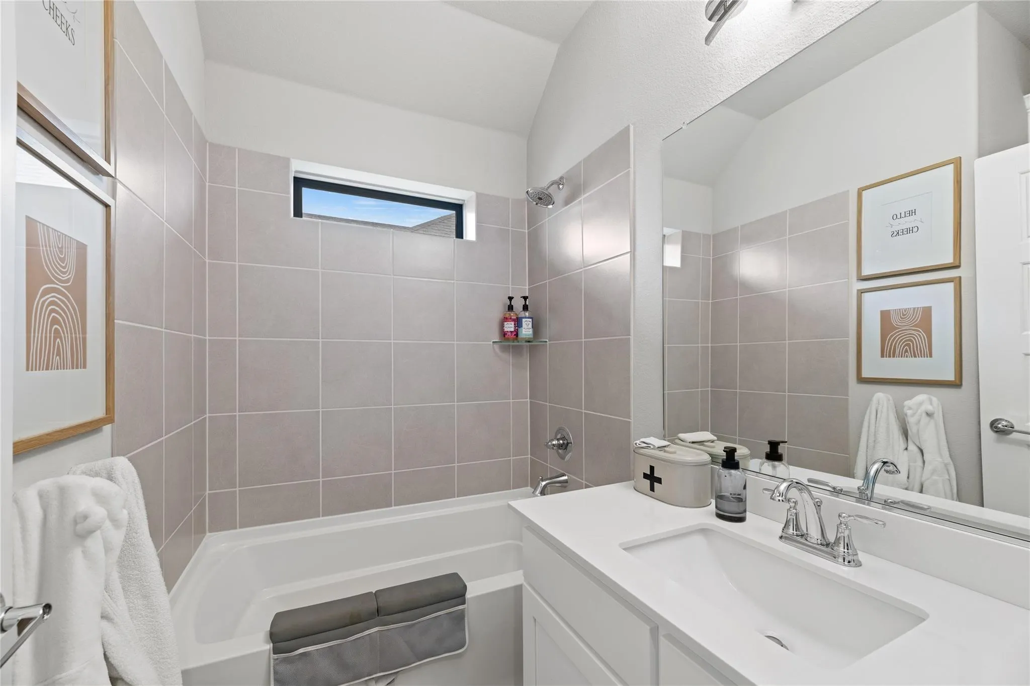Bathtub and shower combination with light-toned tiled walls, white vanity with integrated sink, and chrome fixtures