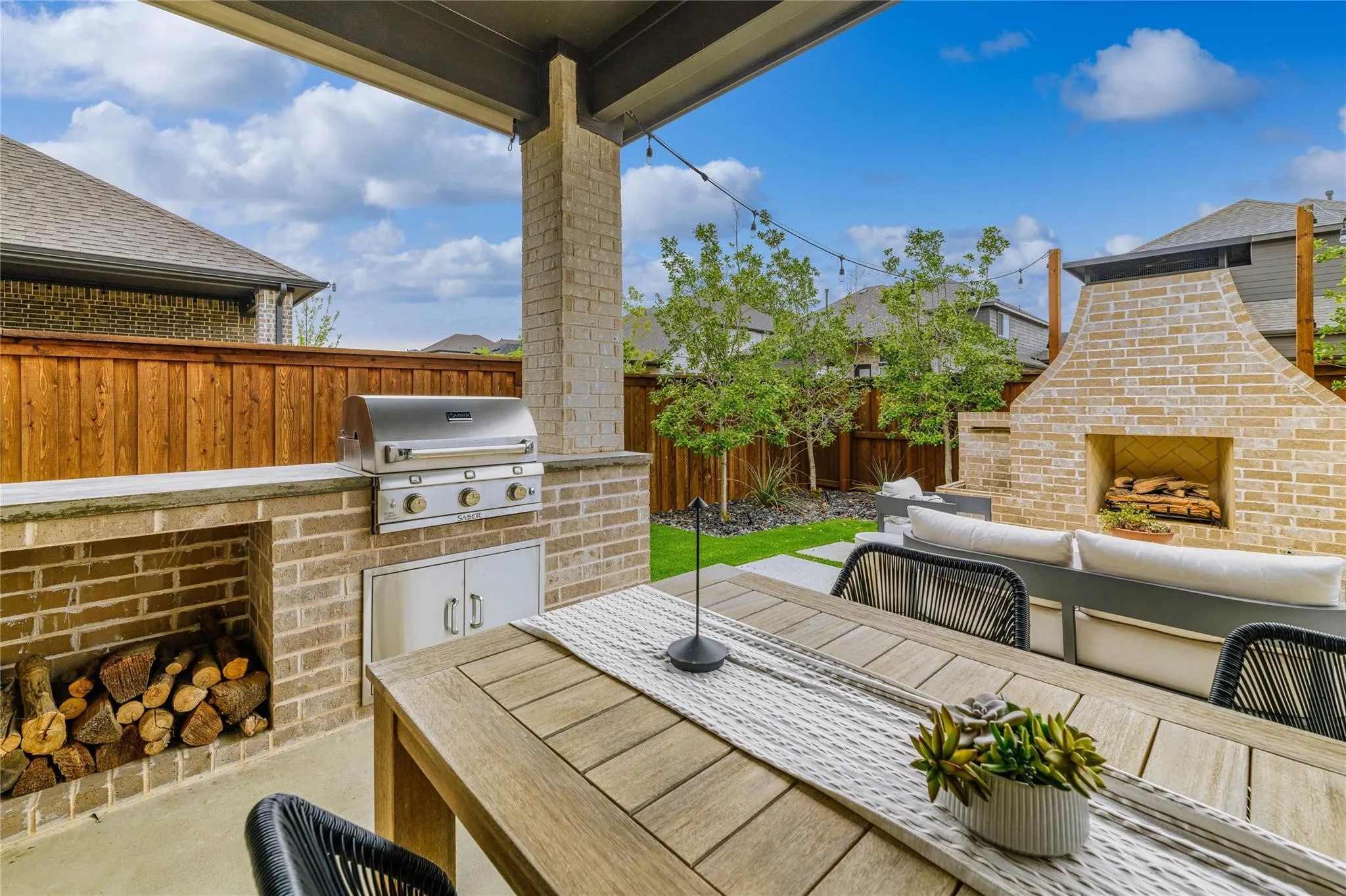 Covered patio featuring an outdoor brick fireplace, built-in brick grilling station with stainless steel grill, and a wood privacy fence