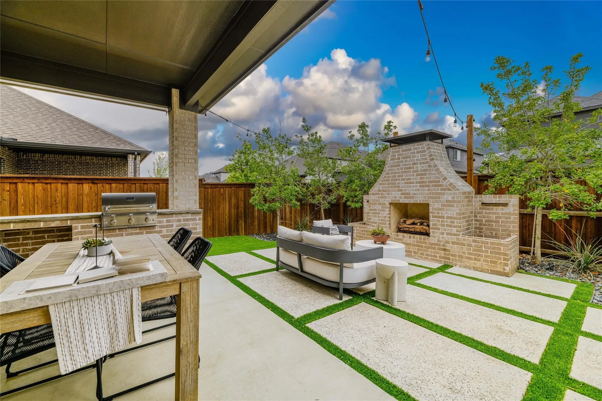 Covered patio featuring an outdoor kitchen with grill, brick fireplace, geometric hardscaping, and artificial turf