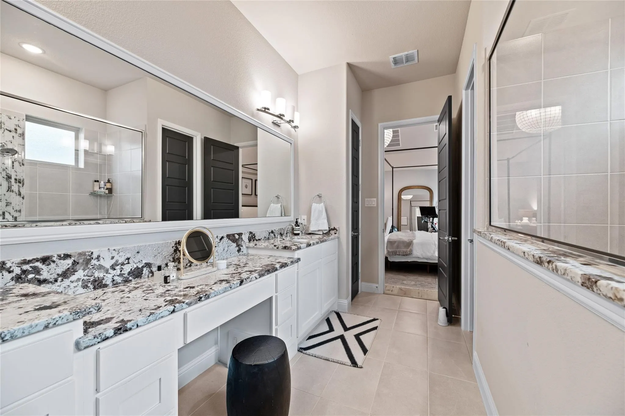 Spacious bathroom featuring a dual vanity with a makeup station, expansive wall-mounted mirror, and a walk-in shower with a glass enclosure