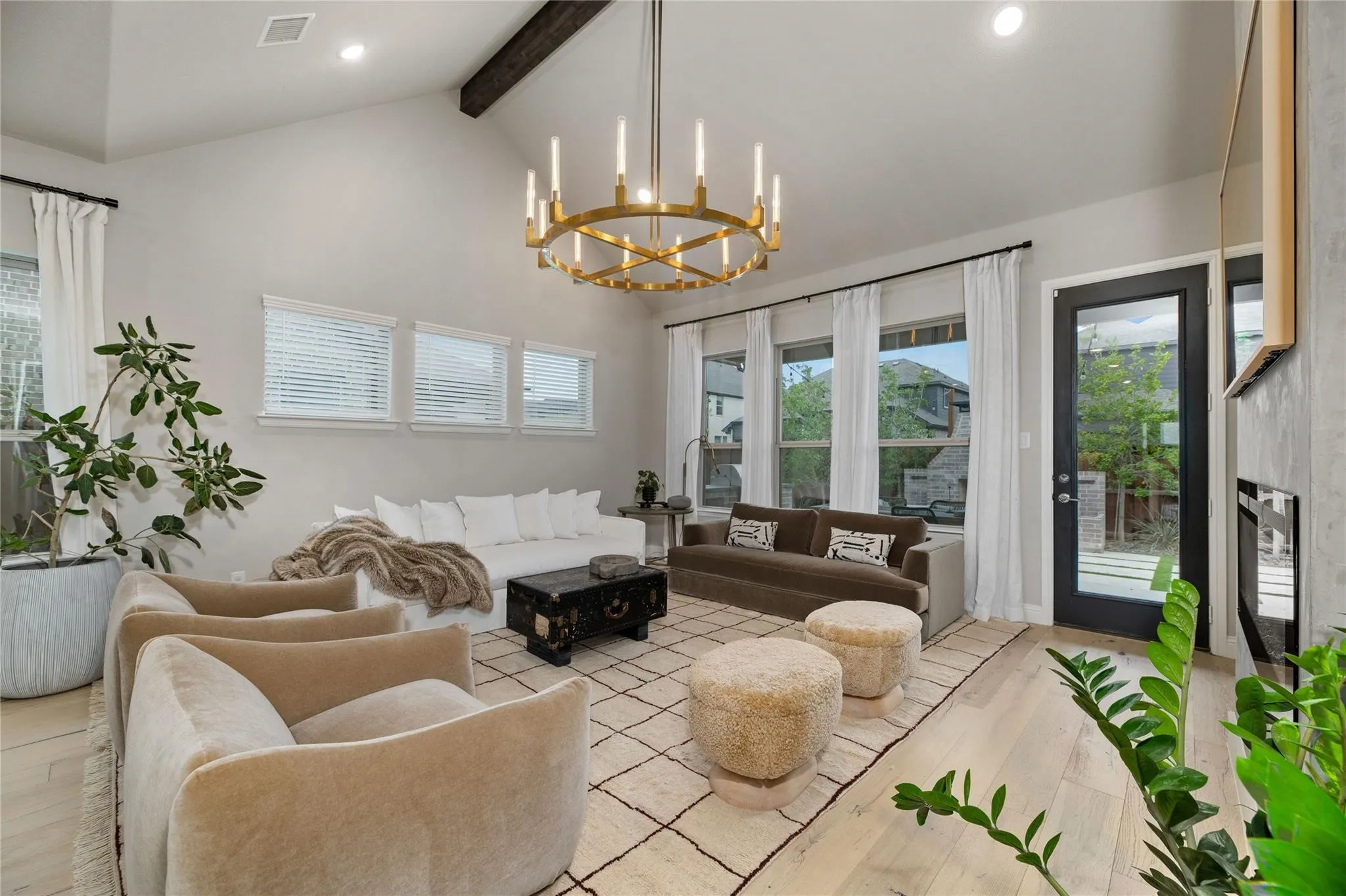 Vaulted ceilings with an exposed wood beam, light wood-finish flooring, a contemporary chandelier, multiple windows with blinds, and a built-in fireplace feature