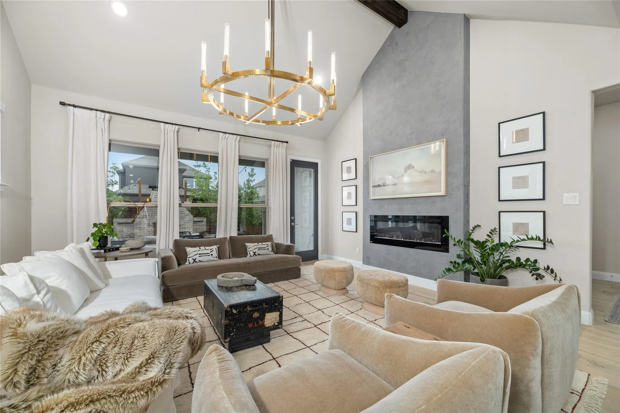 Vaulted ceiling with an exposed beam, linear electric fireplace, full-height accent wall, brass chandelier, and floor-to-ceiling windows