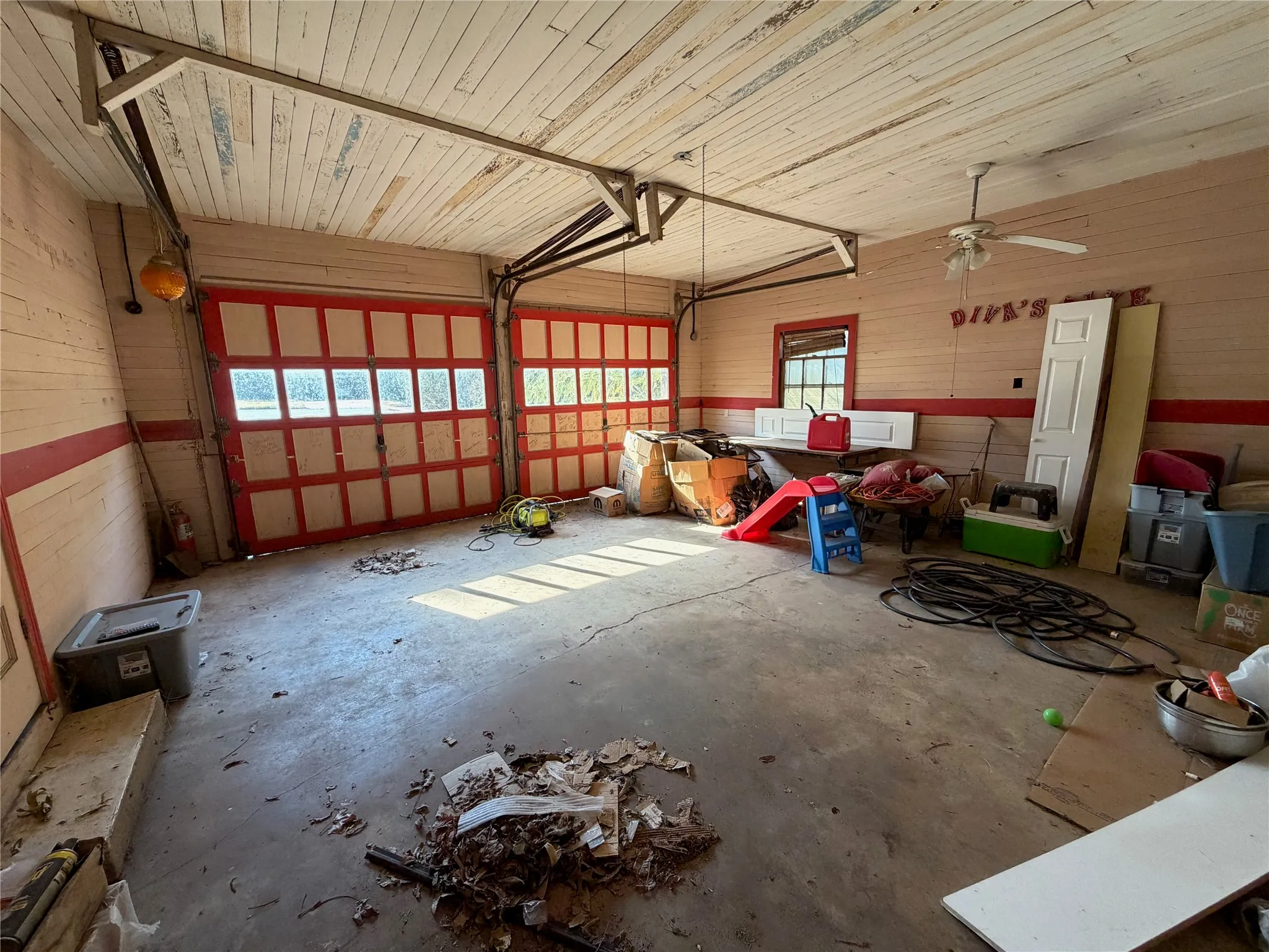 Garage space featuring two paneled garage doors, a concrete floor, and wood-paneled walls and ceiling