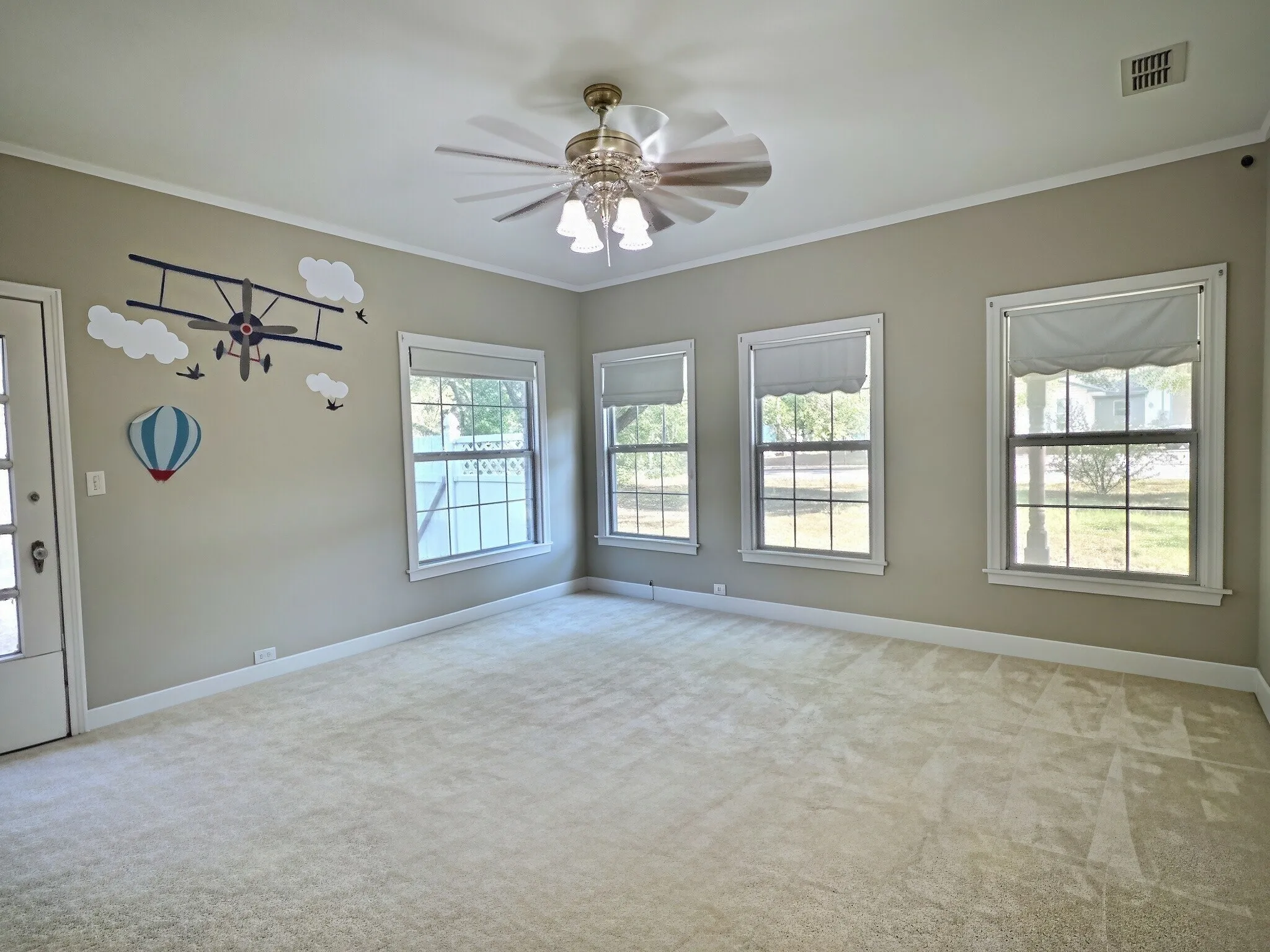 Spacious room featuring light-colored carpeting, multiple windows with white trim, a ceiling fan with integrated lighting, and crown molding