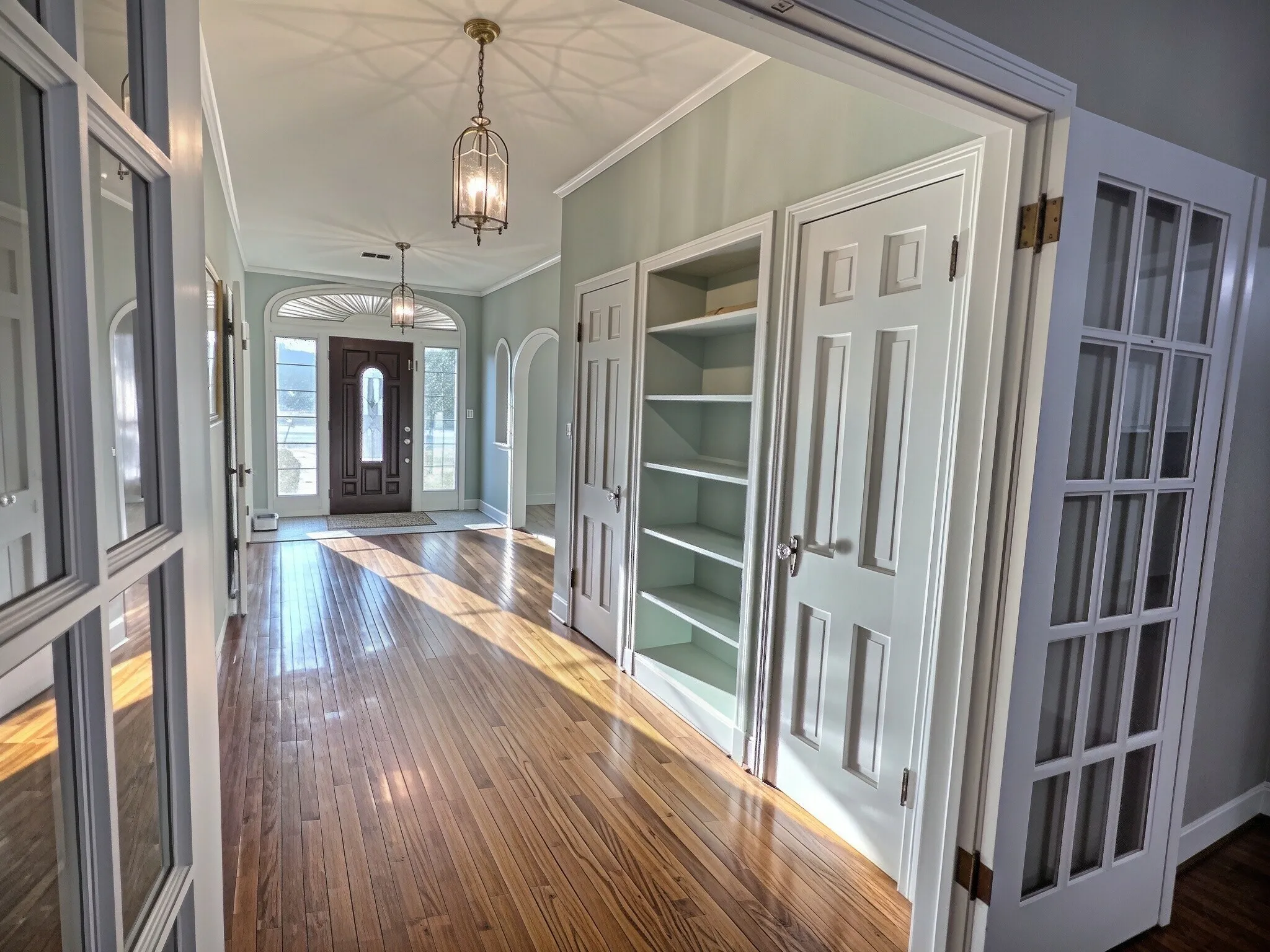 Hardwood flooring throughout, recessed built-in shelving, glass-panel French doors, an arched doorway, and an ornate front door with sidelights