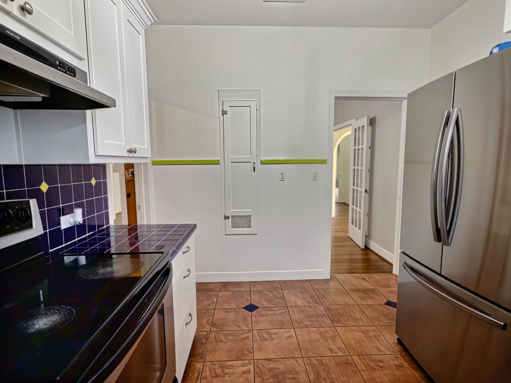 White upper and lower cabinetry, dark tile backsplash, dark tile countertops, and stainless steel appliances