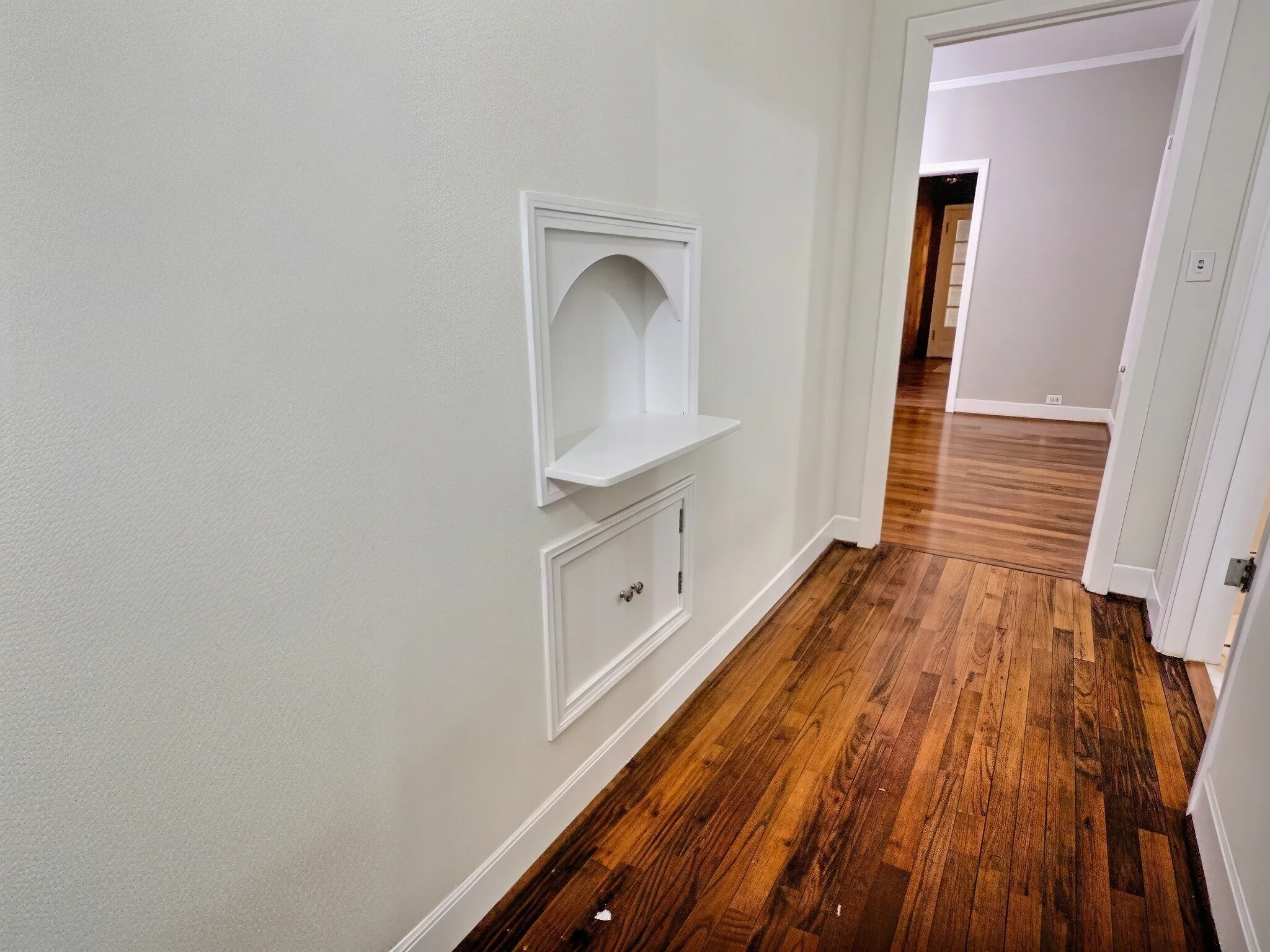 Rich wood-finish flooring throughout, featuring a built-in display nook with integrated shelving and a white panel door