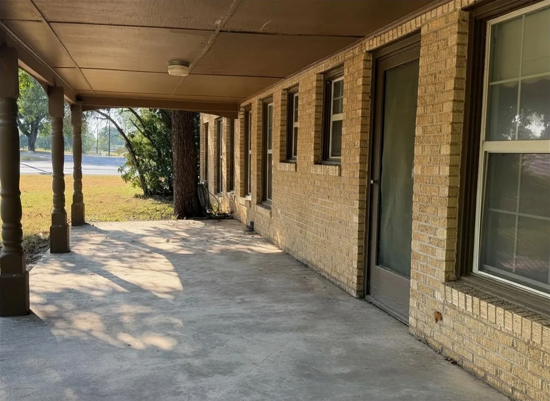 Covered concrete porch with decorative columns, brick exterior, and multiple windows