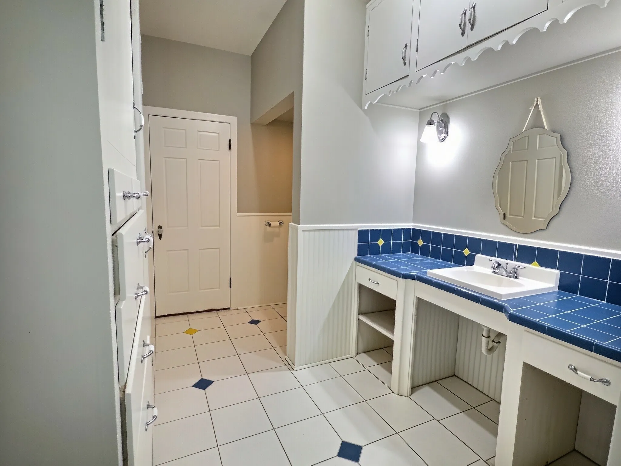 Integrated sink with blue tile countertop, white wall cabinetry, and white beadboard paneling