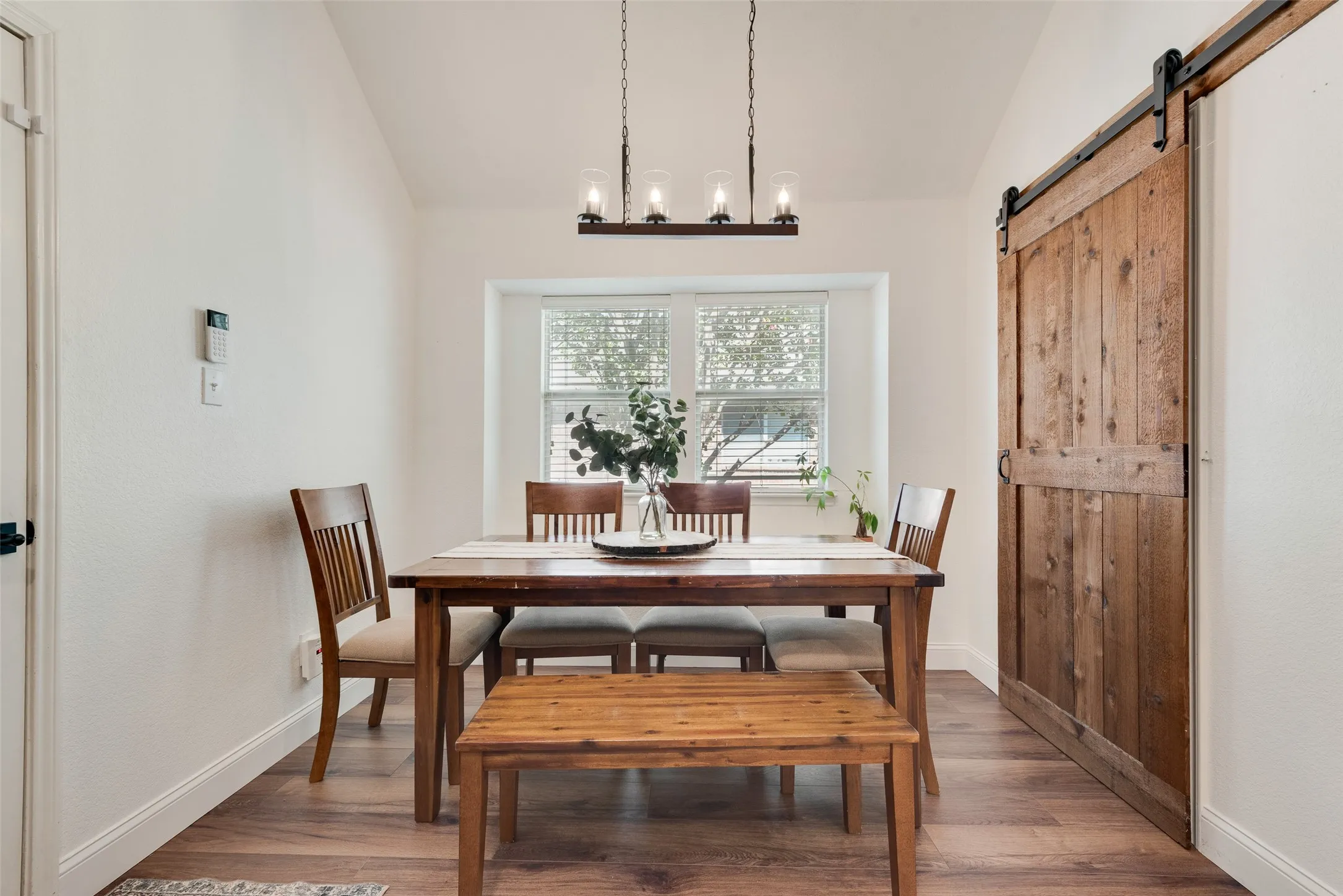 Vaulted ceiling, wood-finish flooring, recessed window, dark wood barn door, and a linear chandelier