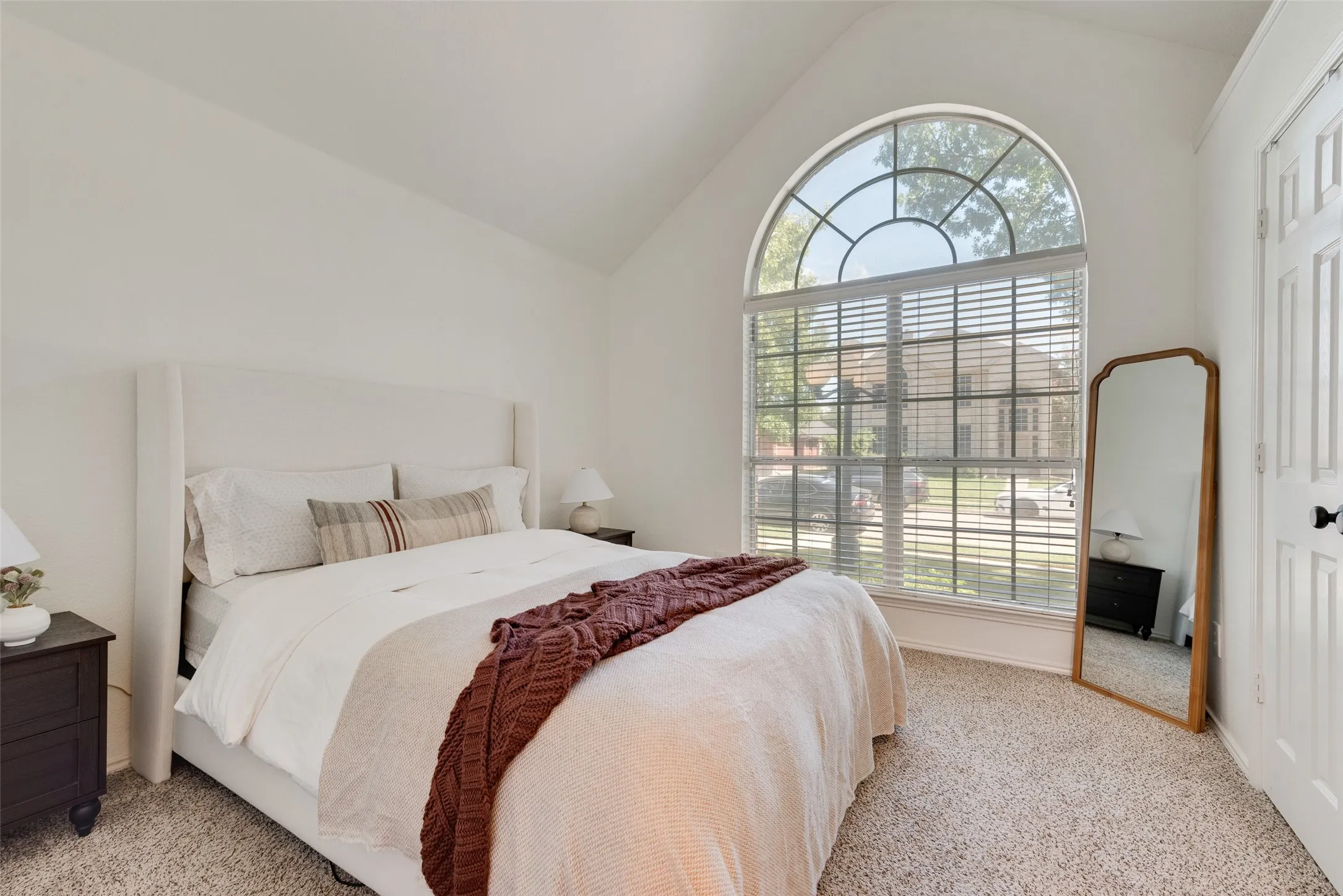 Vaulted ceiling with an arched window featuring interior blinds, carpeting, and a paneled door