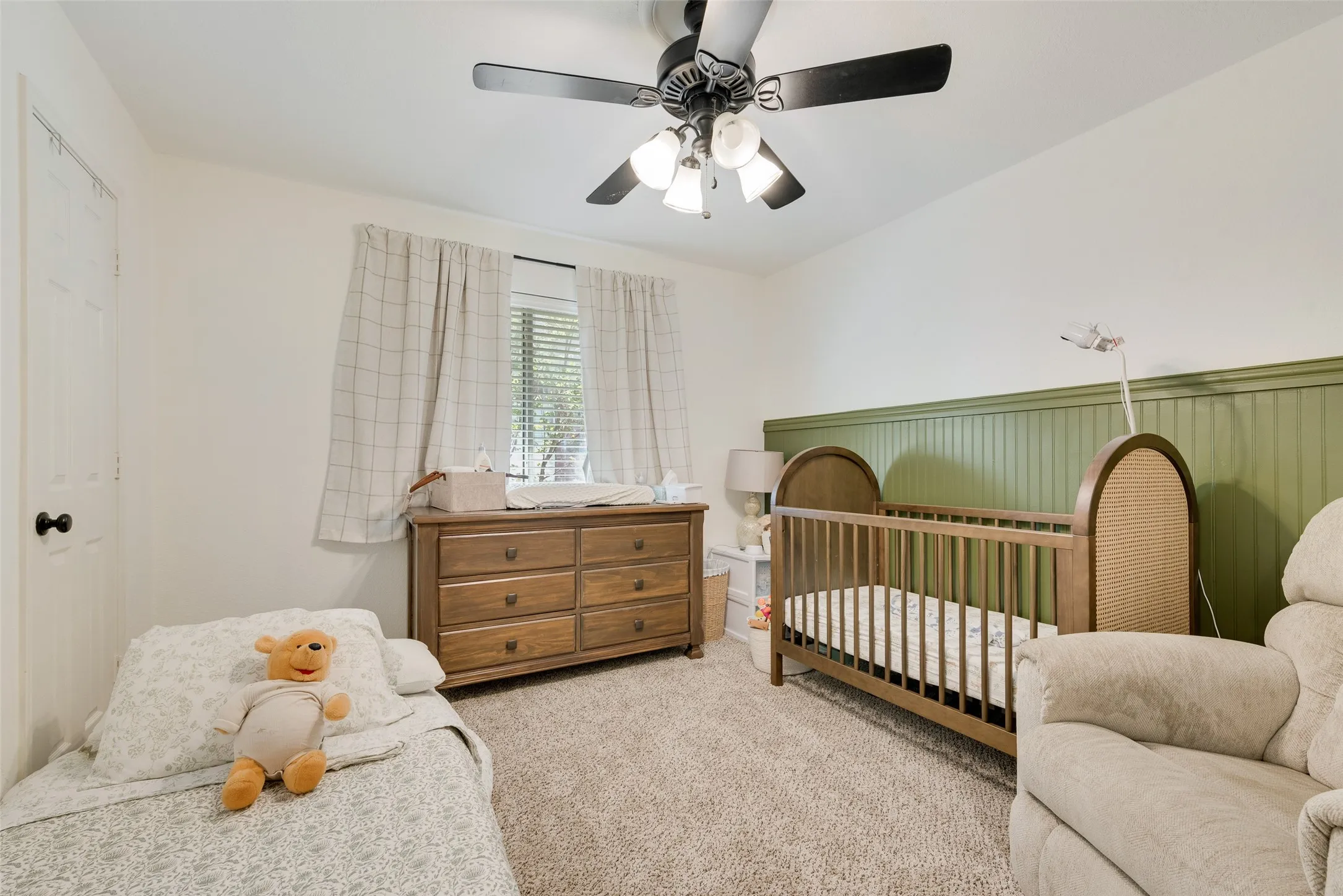 Carpeted room featuring a ceiling fan with light fixture, window with blinds, and green wainscoting