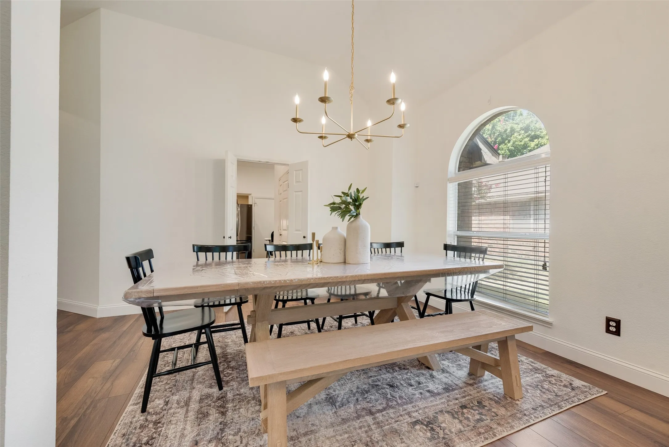 Arched window with blinds, wood-finish flooring, white walls, and a chandelier with candelabra bulbs
