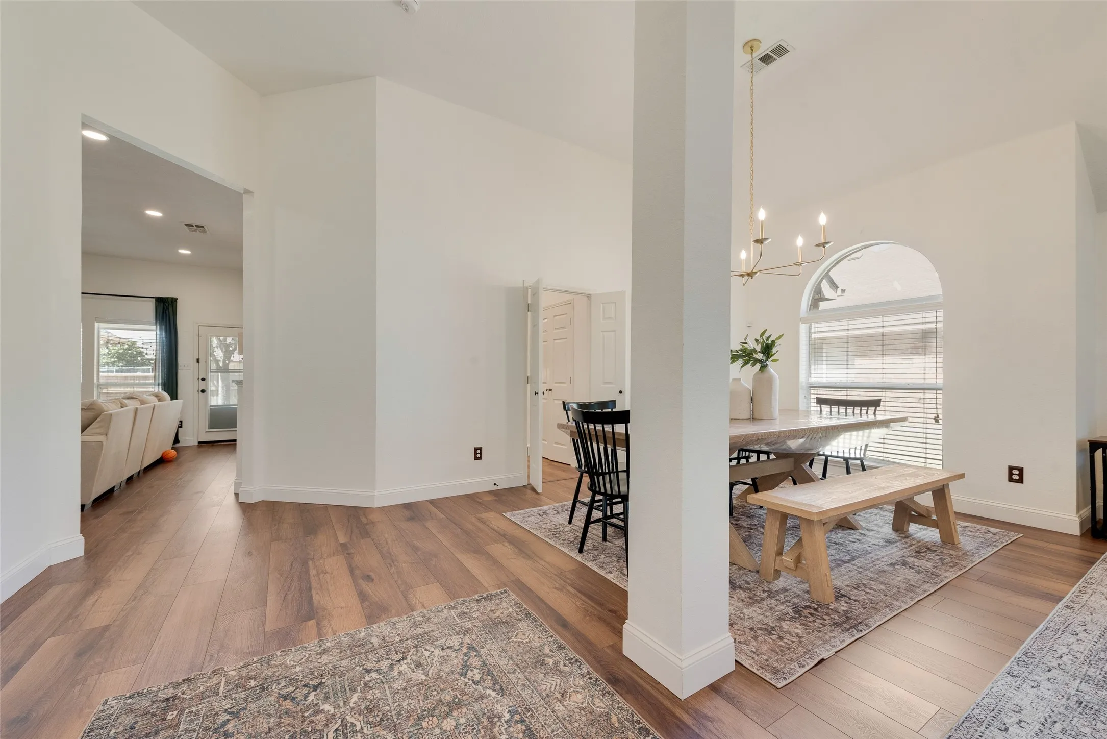 Wood-finish flooring throughout, arched window with horizontal blinds, recessed lighting, and a modern chandelier