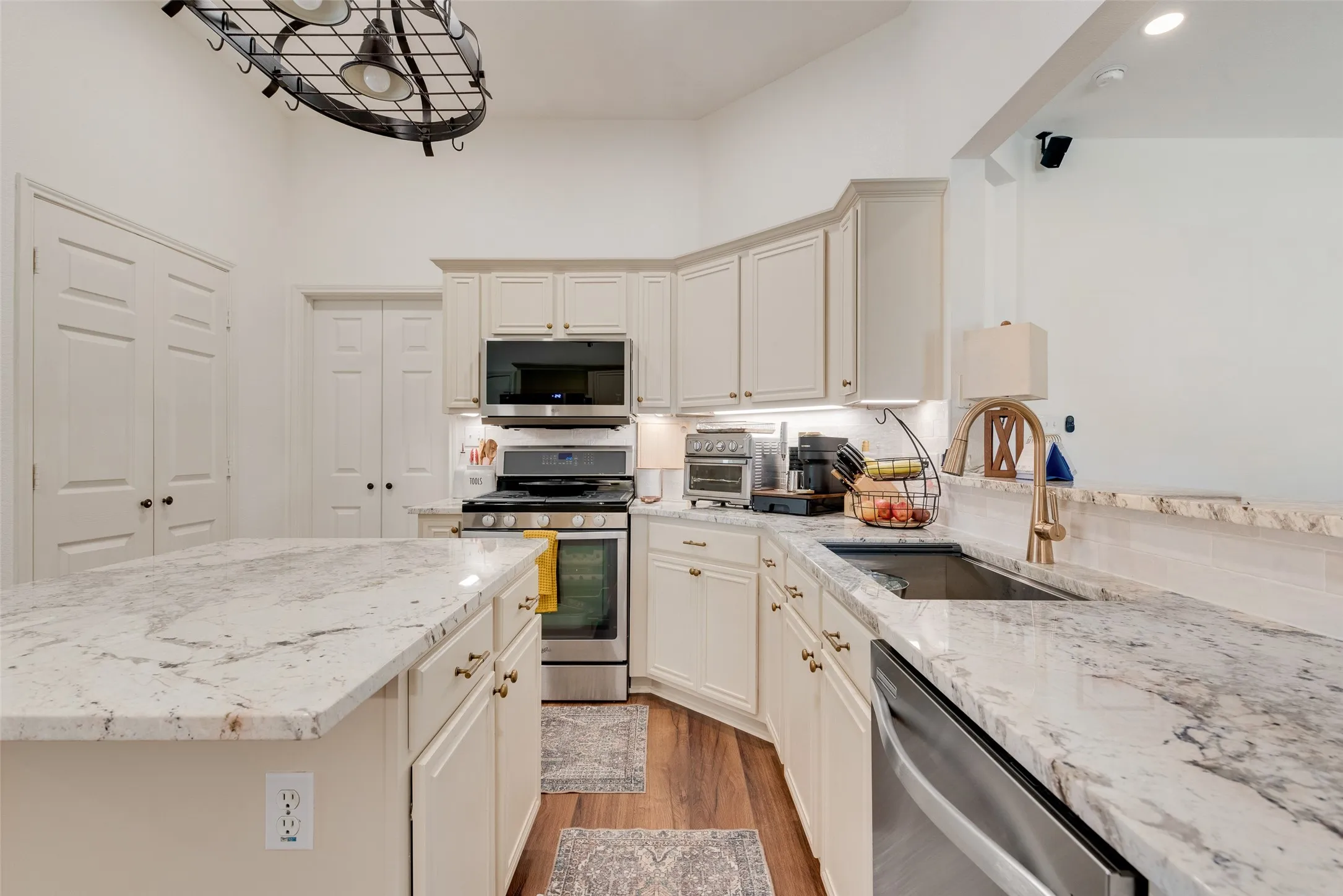 Kitchen featuring an island, light-toned cabinetry, stainless steel appliances, and granite countertops