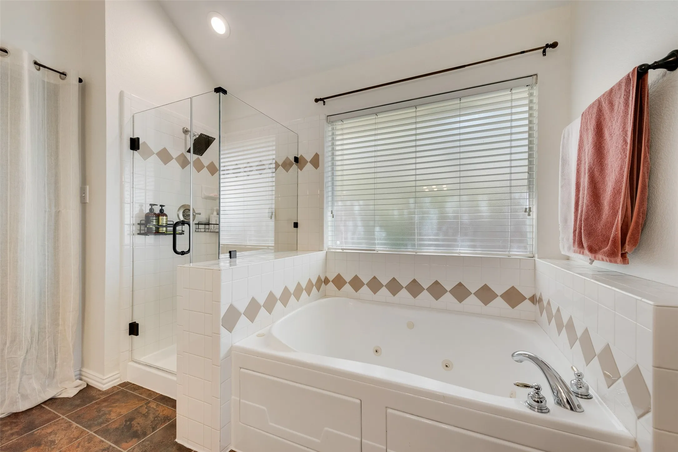 Soaking tub with chrome fixtures, glass-enclosed shower, white tile surround with decorative accents, and recessed ceiling lighting