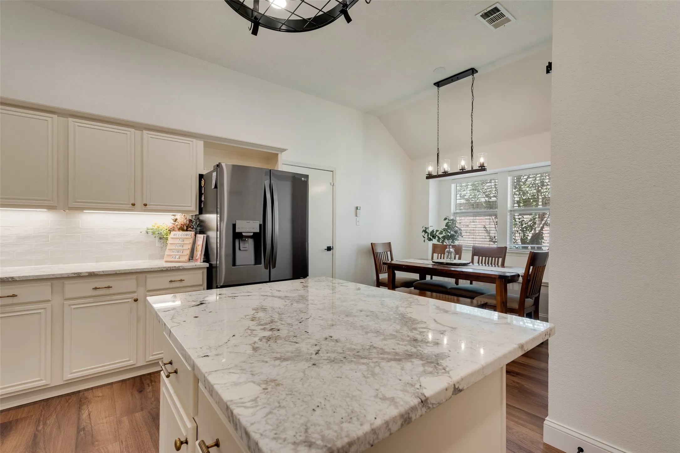 Kitchen featuring a large island with a stone countertop, light-toned cabinetry, and wood-finish flooring