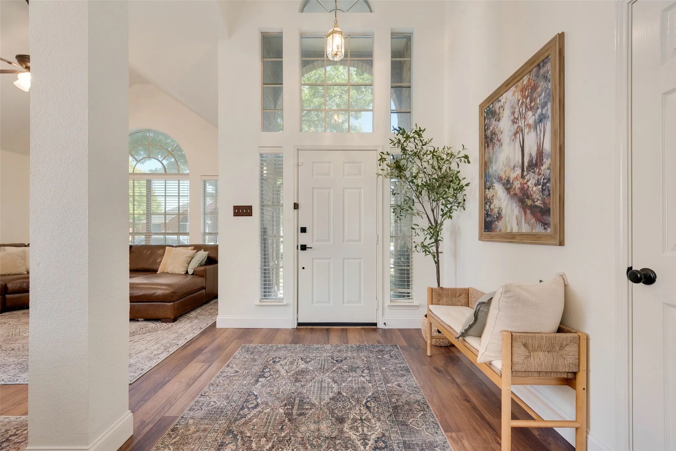 Vaulted ceiling entryway with wood-finish flooring, a white paneled door, and vertical sidelight windows